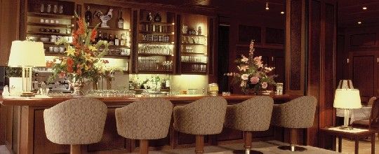 Elegante Bar mit Holzverkleidung, Blumenarrangements und gepolsterten Barhockern.