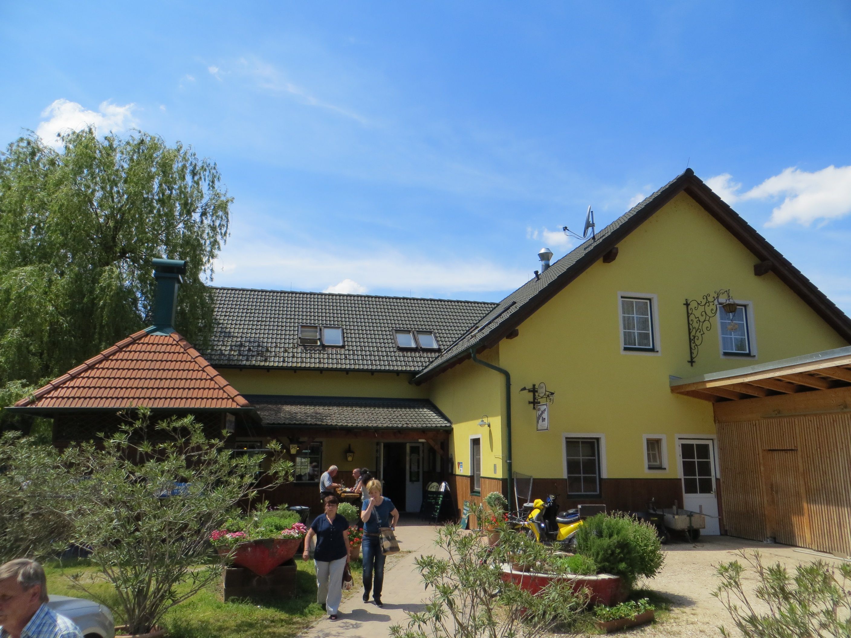 Ein gelbes Gasthaus mit grauem Dach und Garten im Vordergrund.
