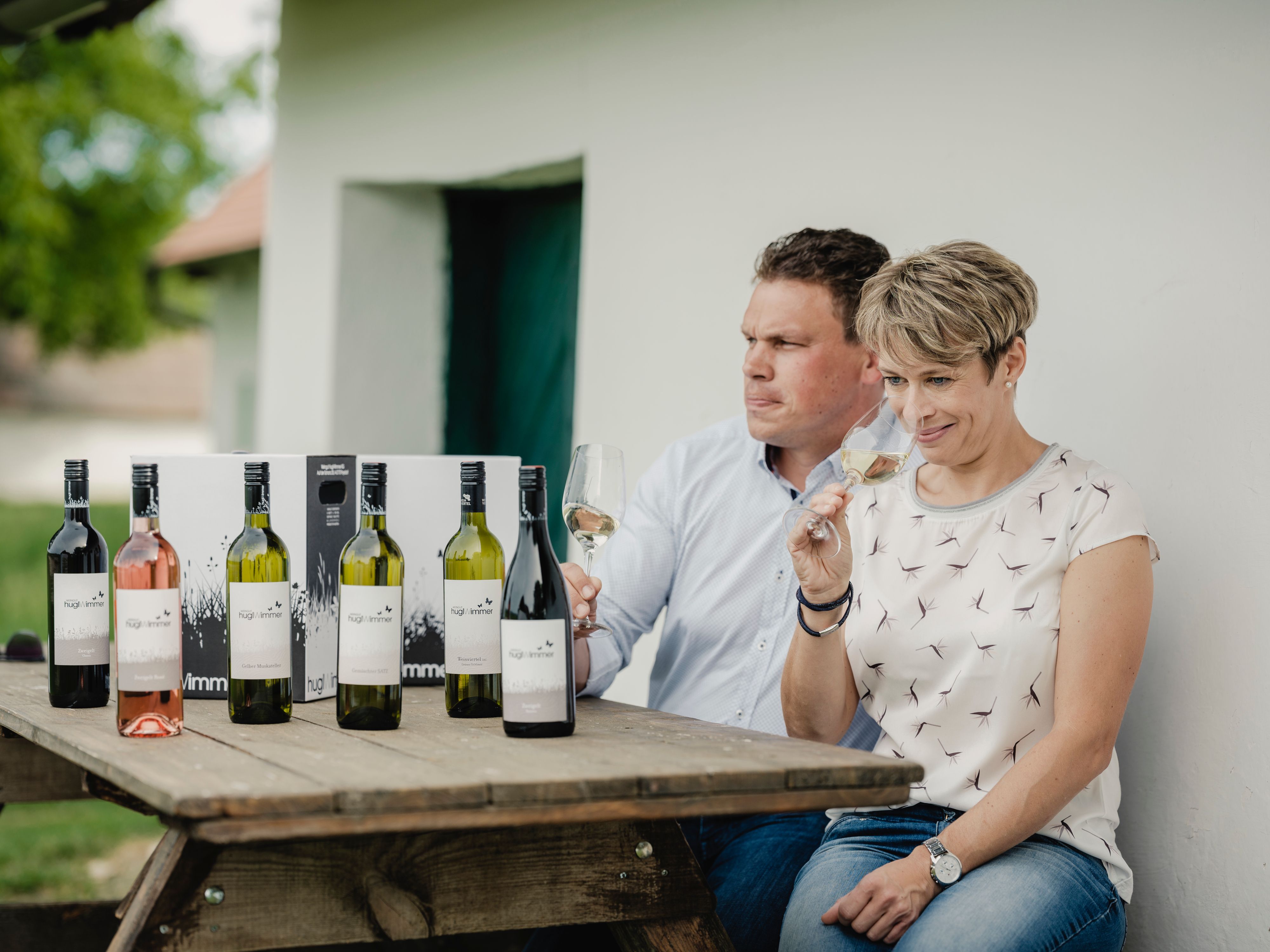 Zwei Personen sitzen an einem Tisch mit Weinflaschen und probieren Wein.