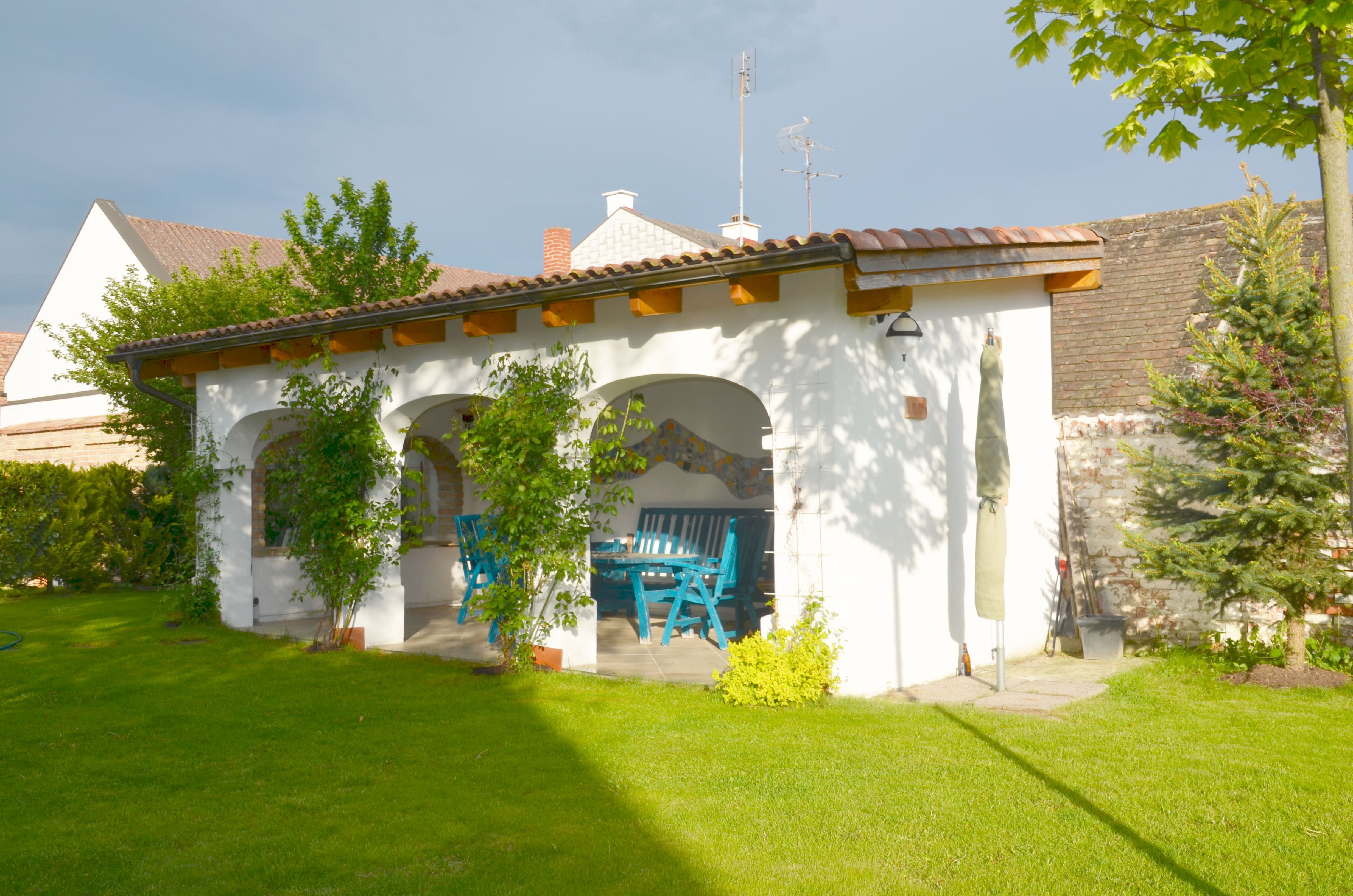 Ein Garten mit einer überdachten Terrasse, blauen Möbeln und grüner Vegetation.