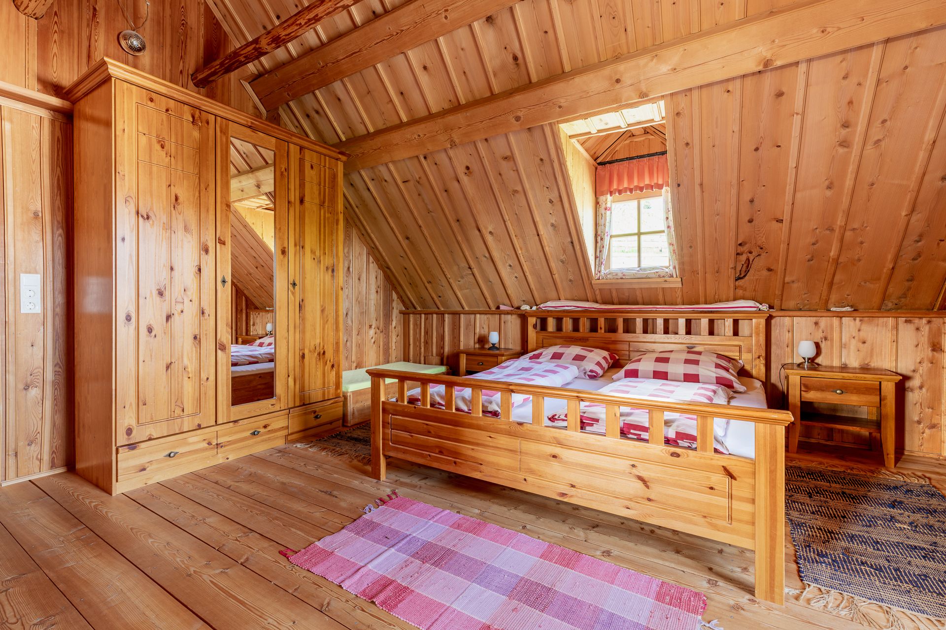 Schlafzimmer mit Holzvertäfelung, großem Doppelbett, Holzkasten, Teppichen und einem Fenster.