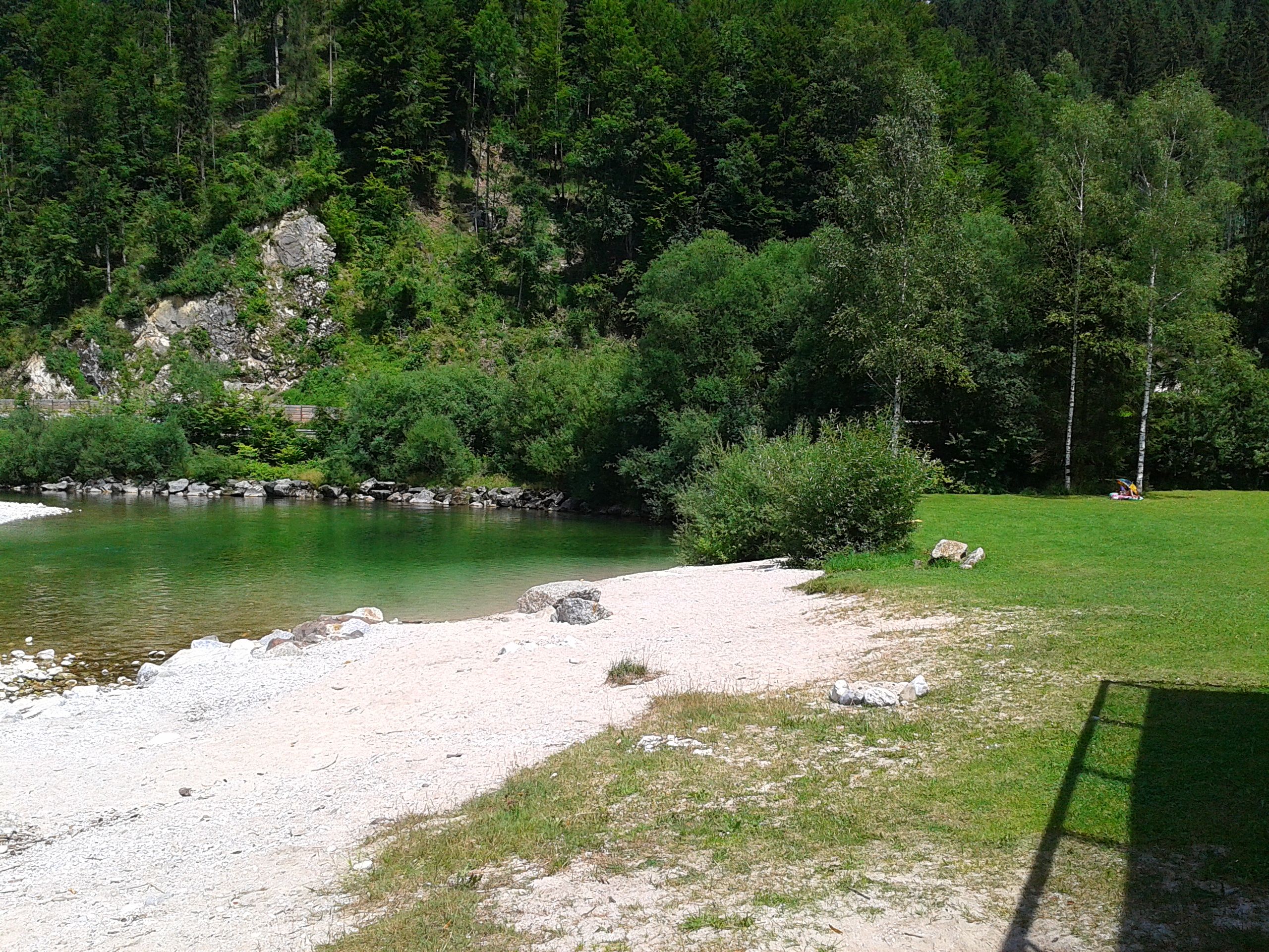 Ein Fluss mit klarem Wasser, umgeben von grünen Bäumen und einer kleinen Kiesfläche am Ufer.