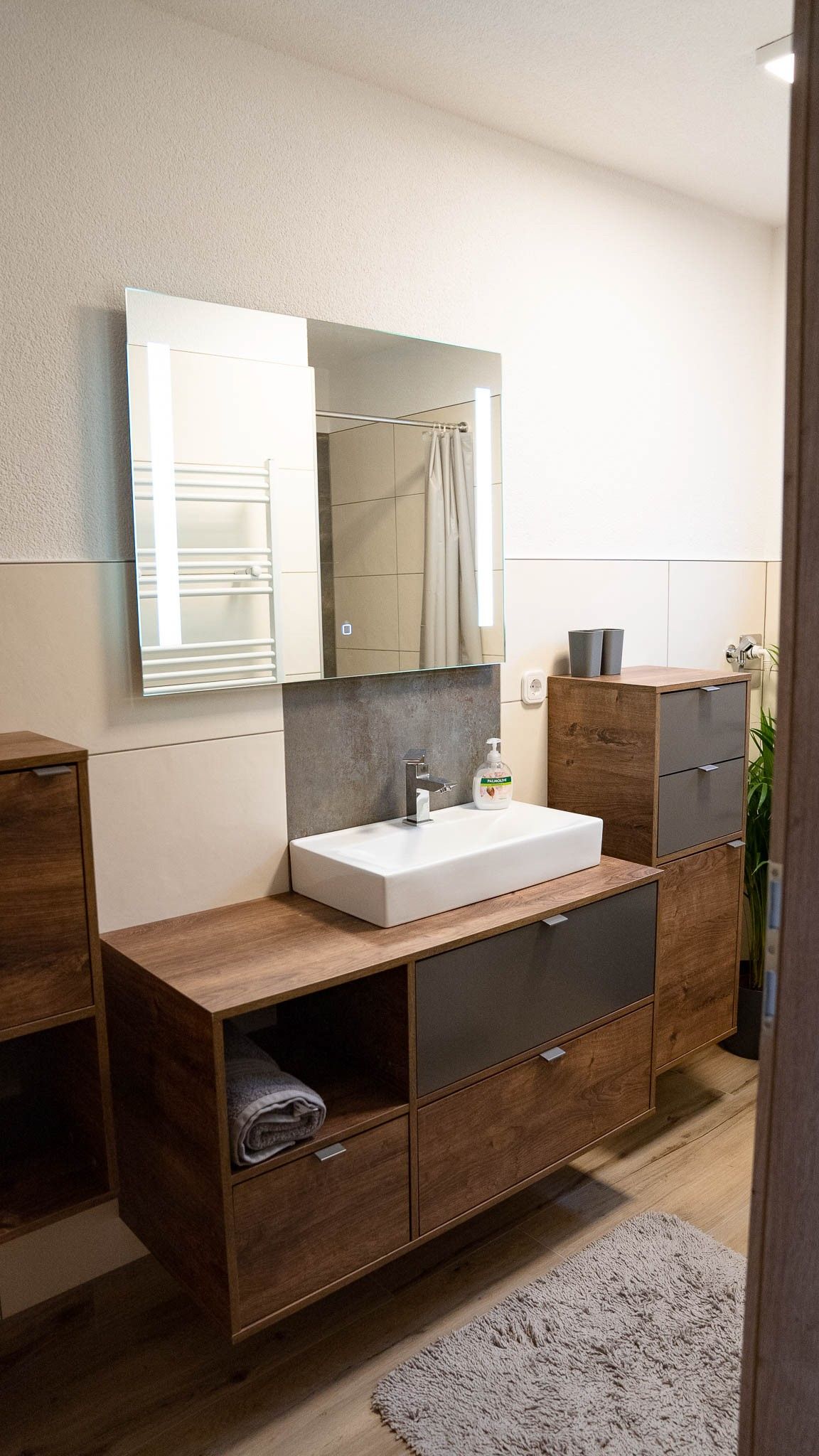 Modernes Badezimmer mit Holzschränken, Waschbecken und Spiegel.