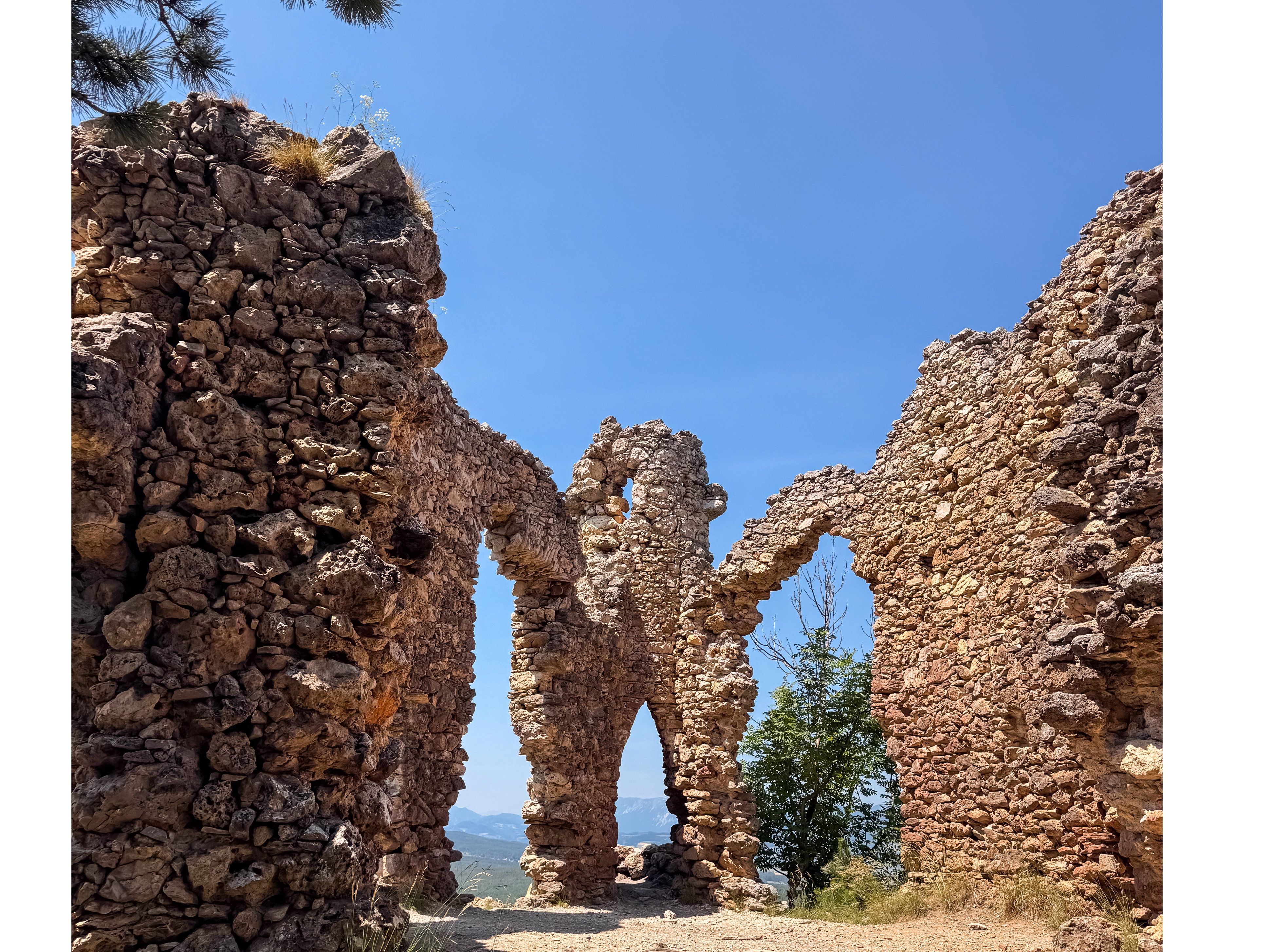 Ruinen einer alten Steinmauer mit Bögen unter blauem Himmel.