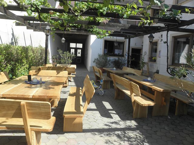 Holzterrasse mit Tischen und Bänken unter einer Pergola mit Weinreben.