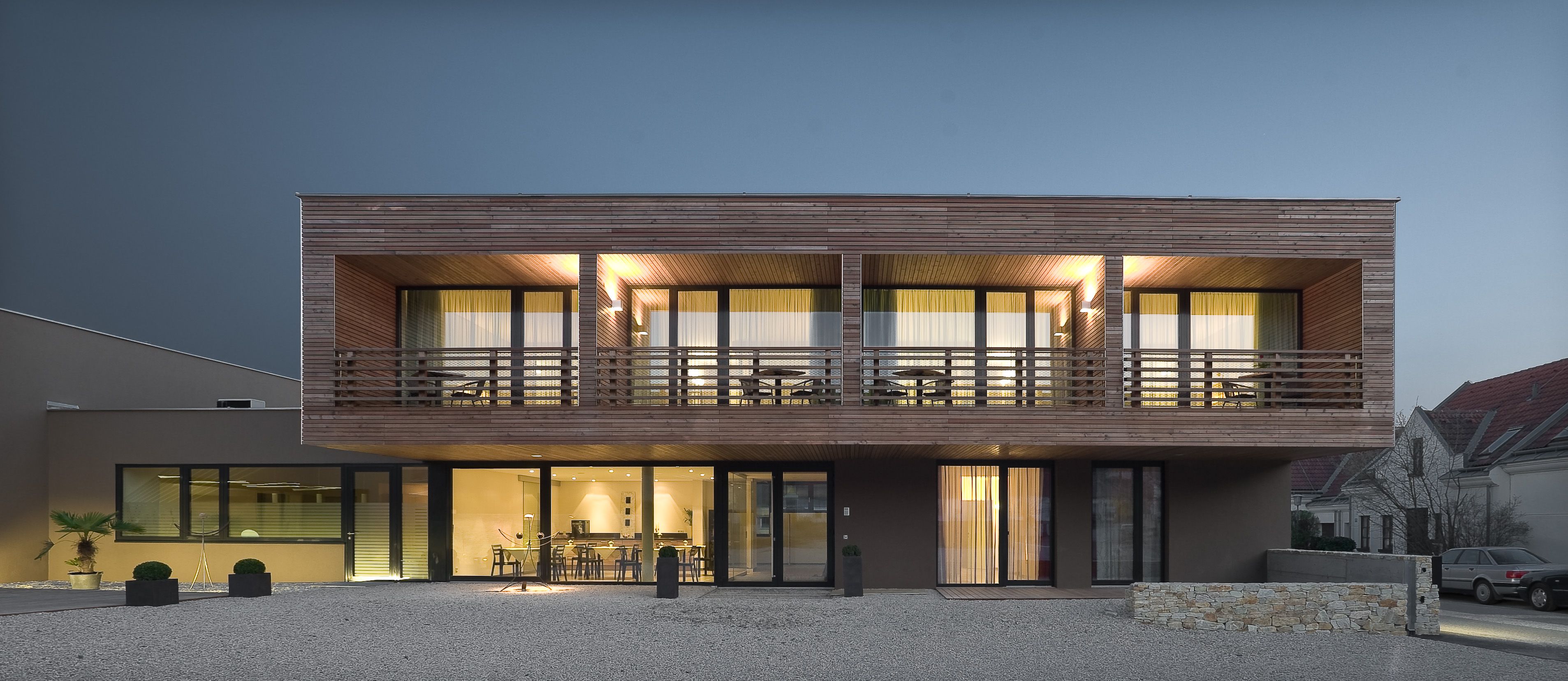 Modernes zweistöckiges Haus mit Holzverkleidung und großen Fenstern bei Nachtbeleuchtung.