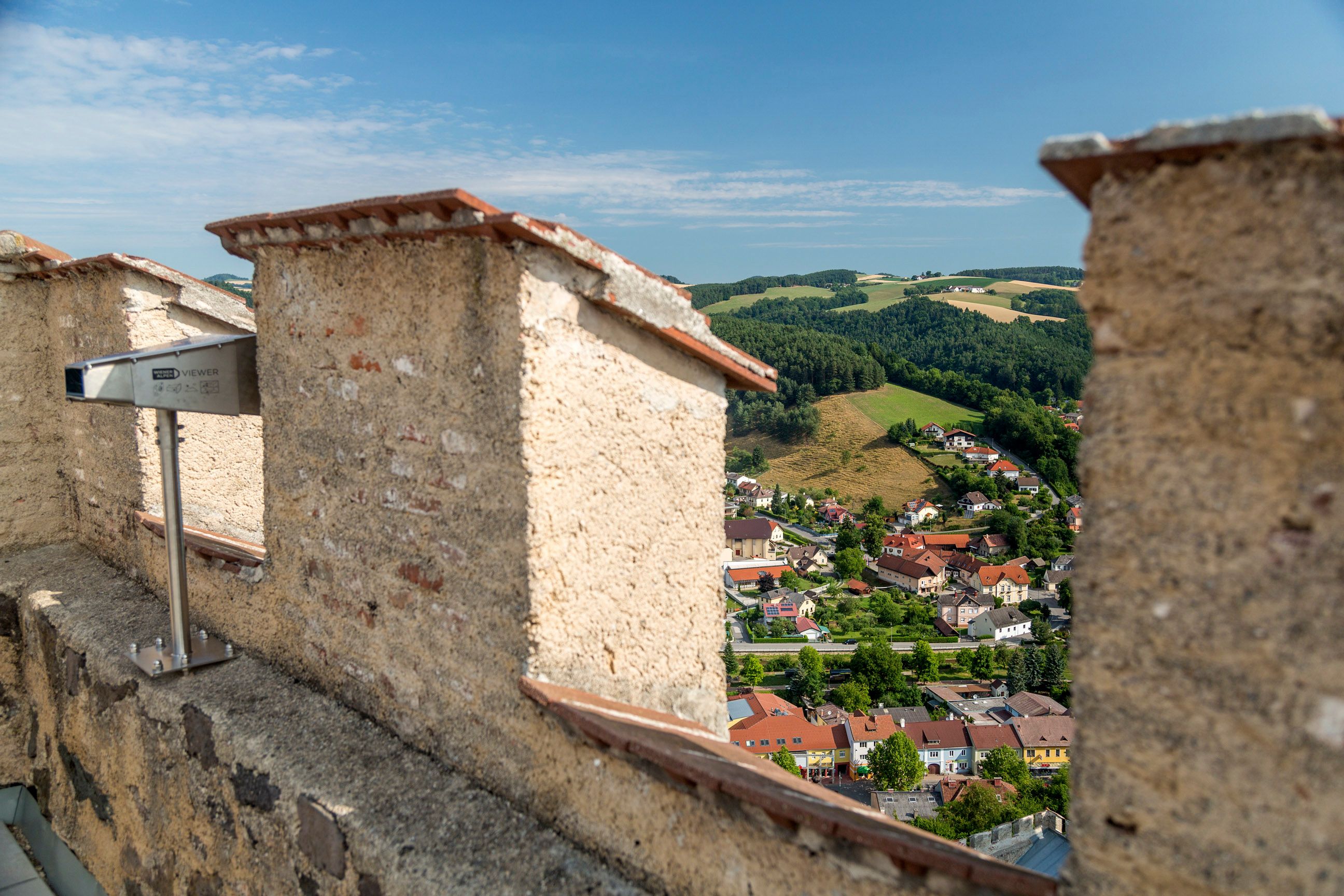 Aussicht von einer Burgruine auf eine Stadt und grüne Hügel.