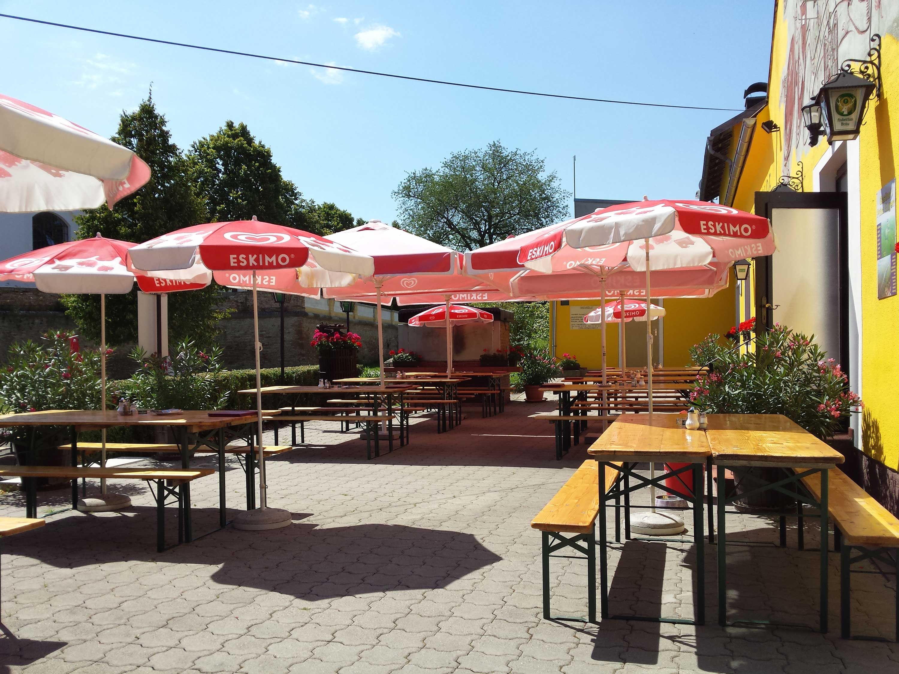 Sonnige Terrasse mit Holzbänken und roten Sonnenschirmen.