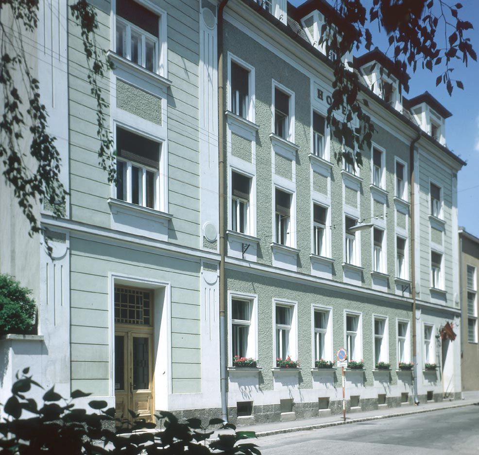 Außenansicht eines mehrstöckigen Gebäudes mit grüner Fassade und weißen Fensterrahmen.