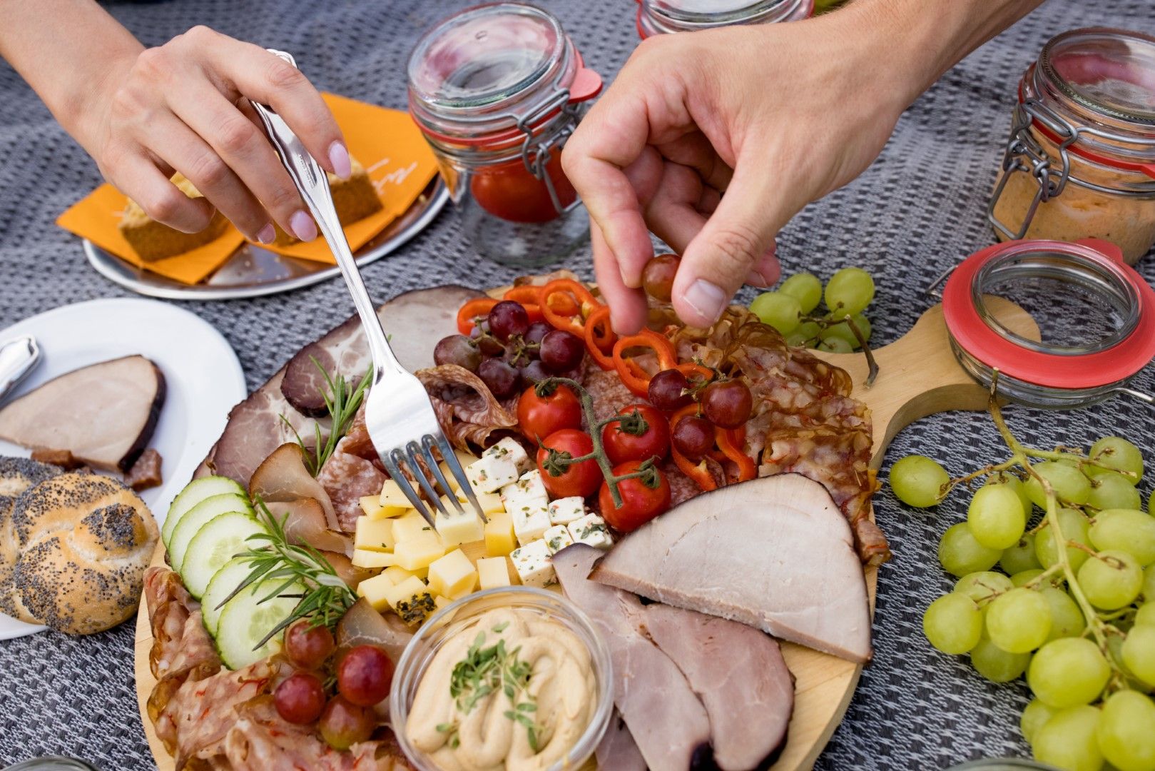 Nahaufnahme einer Jause mit Wurst, Käse, Trauben und Tomaten auf einem Holzteller.