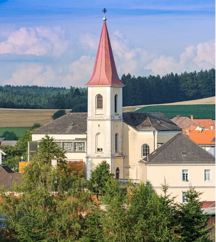 Pfarrkirche Hochwolkersdorf mit rotem, spitzen Turmdach und umliegender Landschaft.