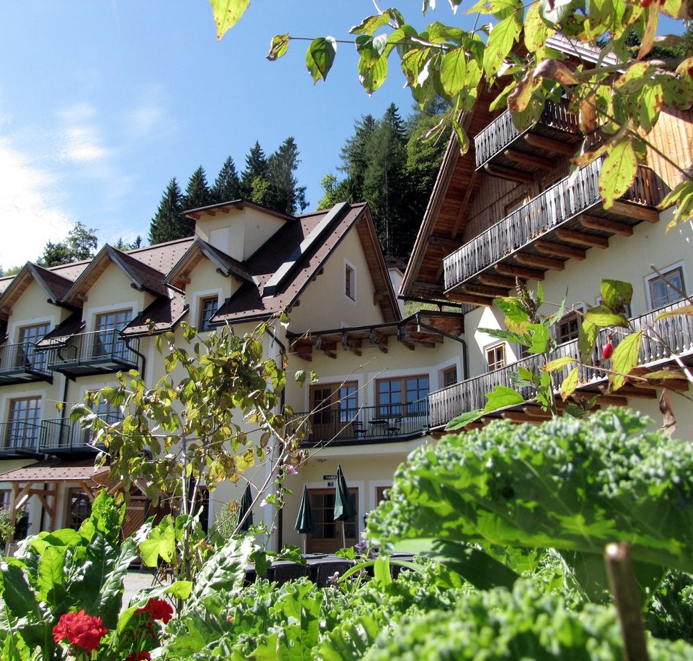 Ein Gebäude im alpinen Stil mit Balkonen, umgeben von üppigem Grün und Pflanzen.