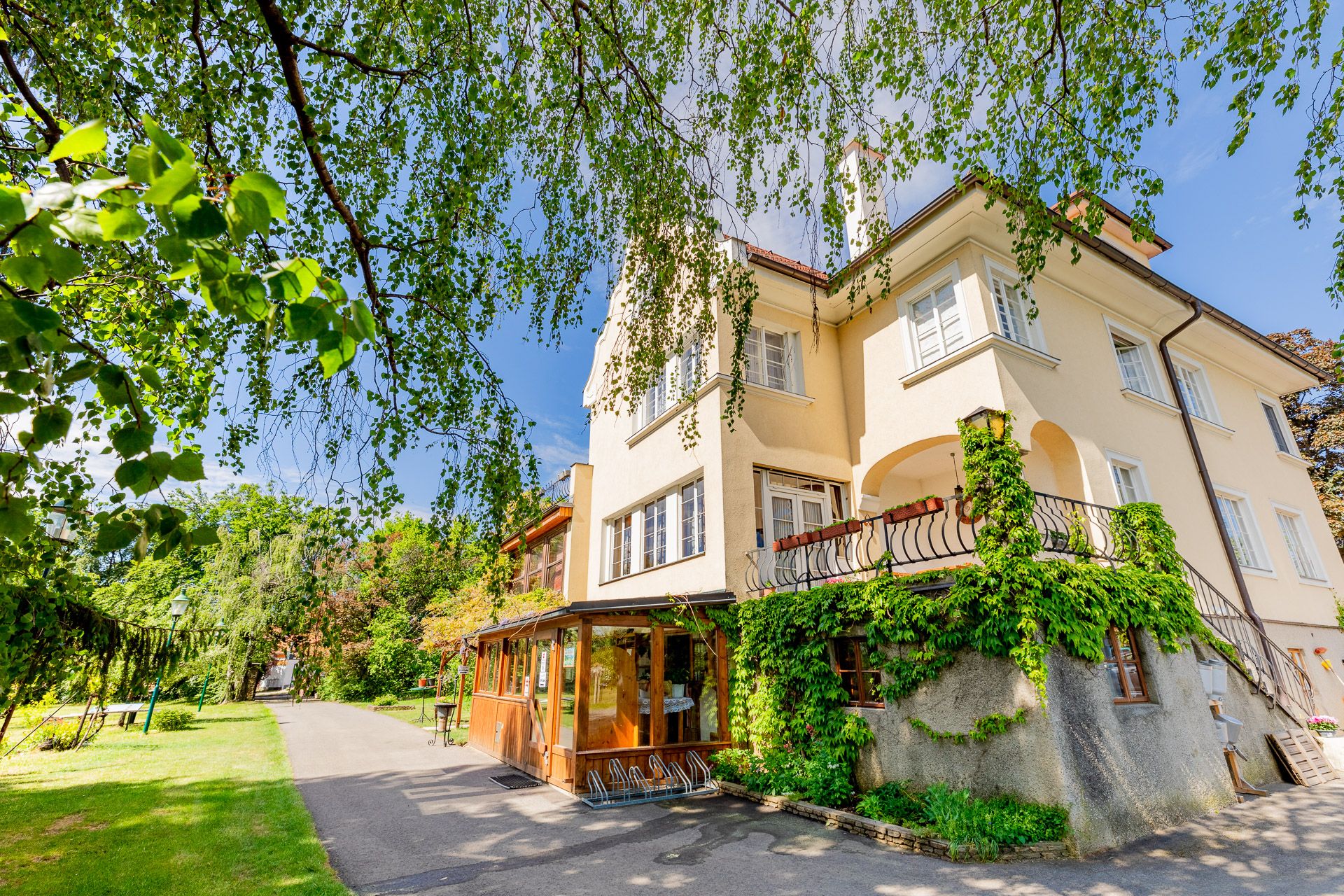 Ein gelbes Herrenhaus mit Efeu bewachsen, umgeben von Bäumen und einem Gartenweg.