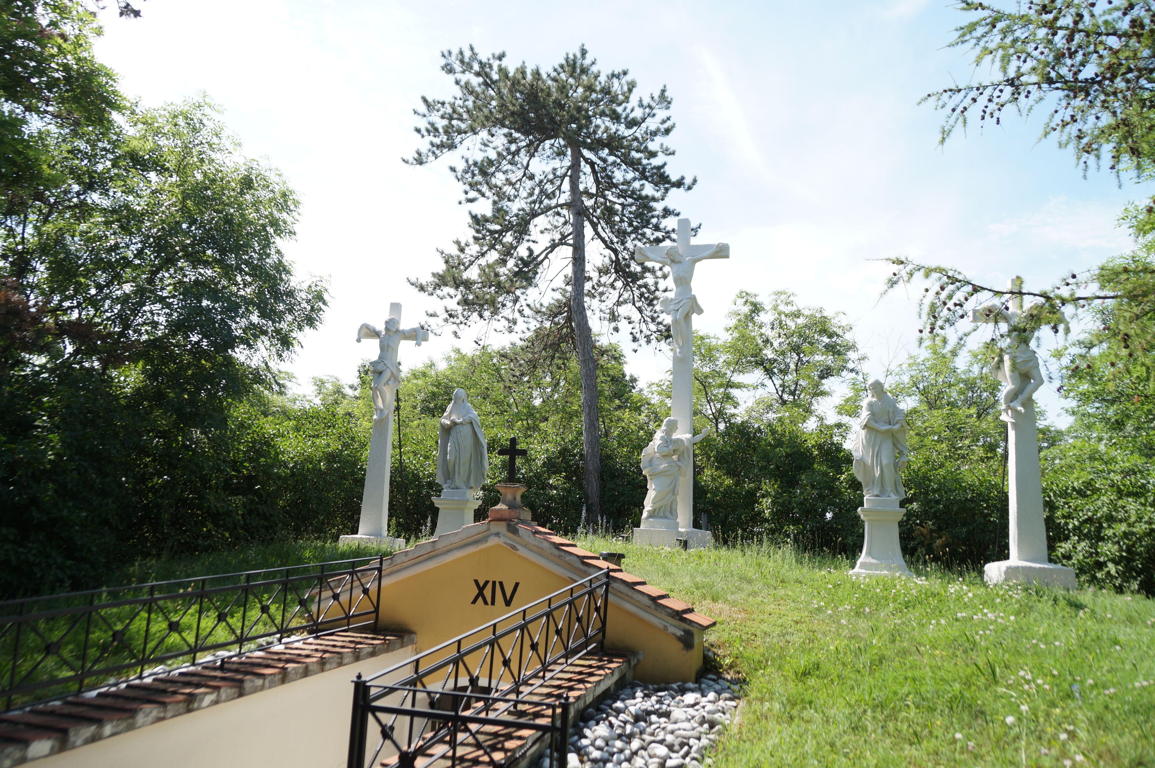 Kreuzwegstation mit mehreren weißen Statuen und einem Kreuz im Freien.