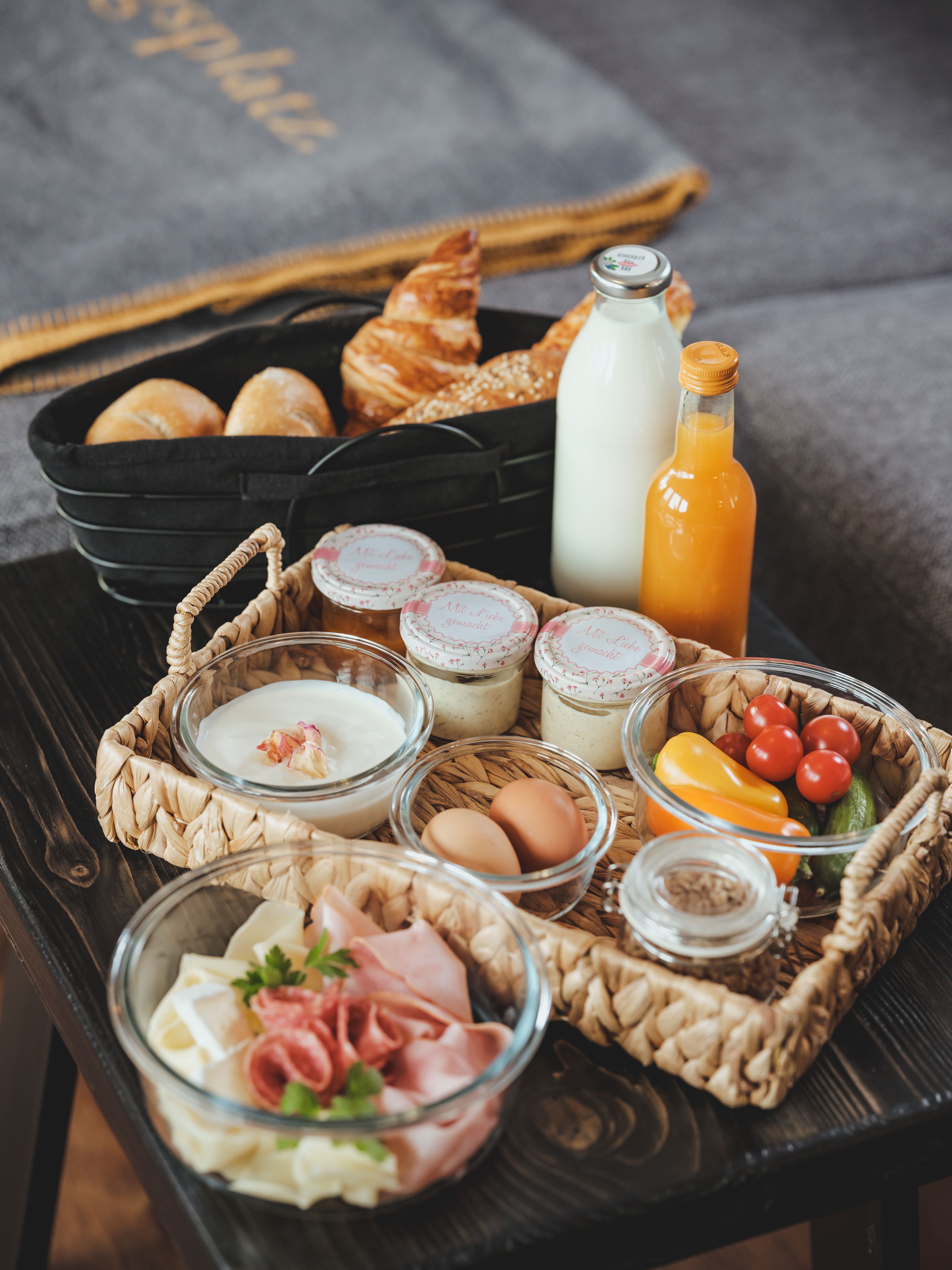 Frühstückstablett mit Brötchen, Croissant, Milch, Saft, Joghurt, Eiern, Aufschnitt und Gemüse.