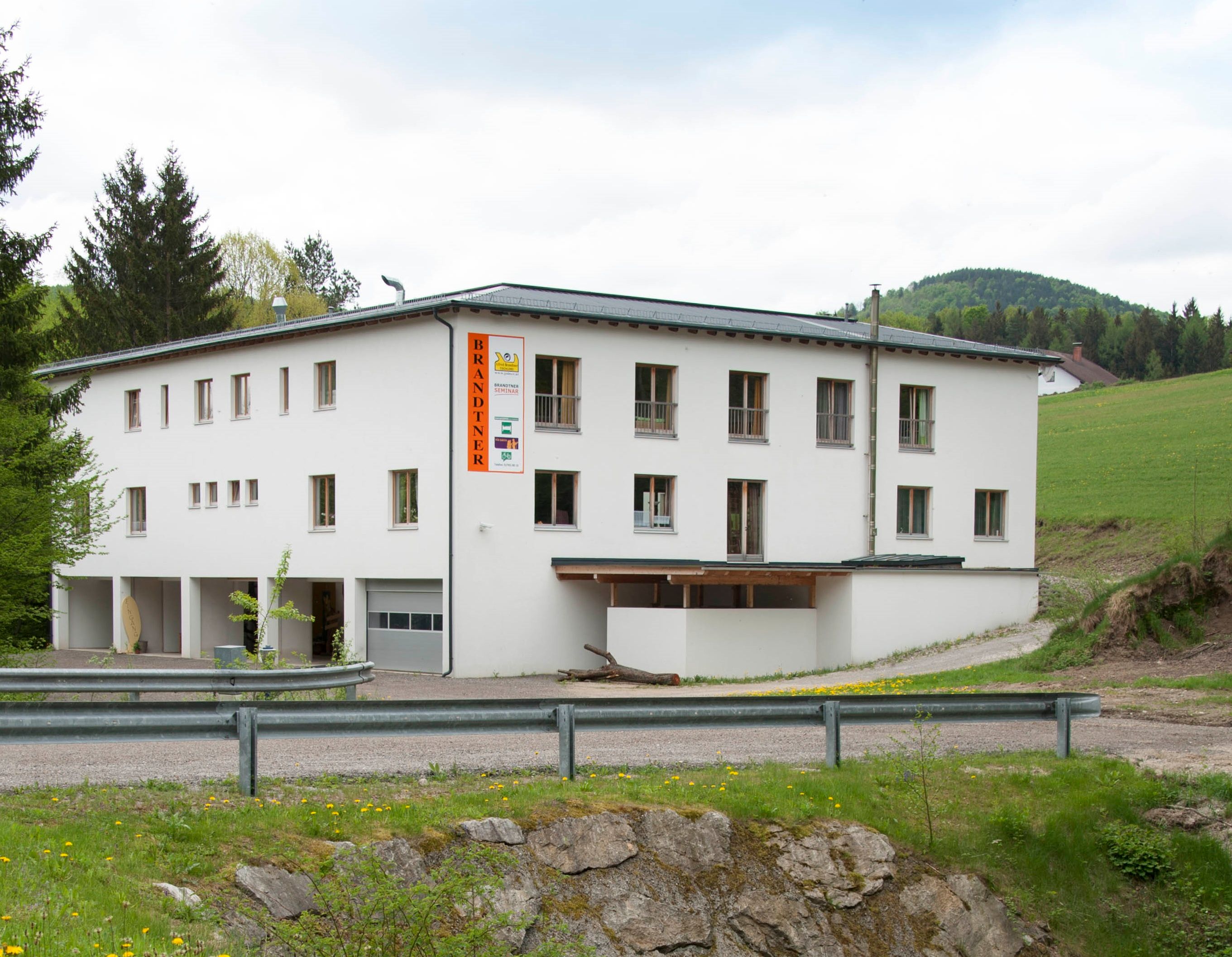 Ein weißes Gebäude mit der Aufschrift 'Brandtner' in ländlicher Umgebung.