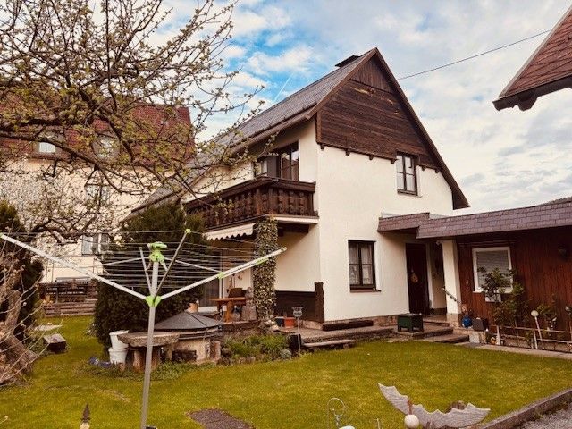 Ein zweistöckiges Haus mit Balkon und Garten, umgeben von Bäumen und einem Wäschetrockner im Vordergrund.