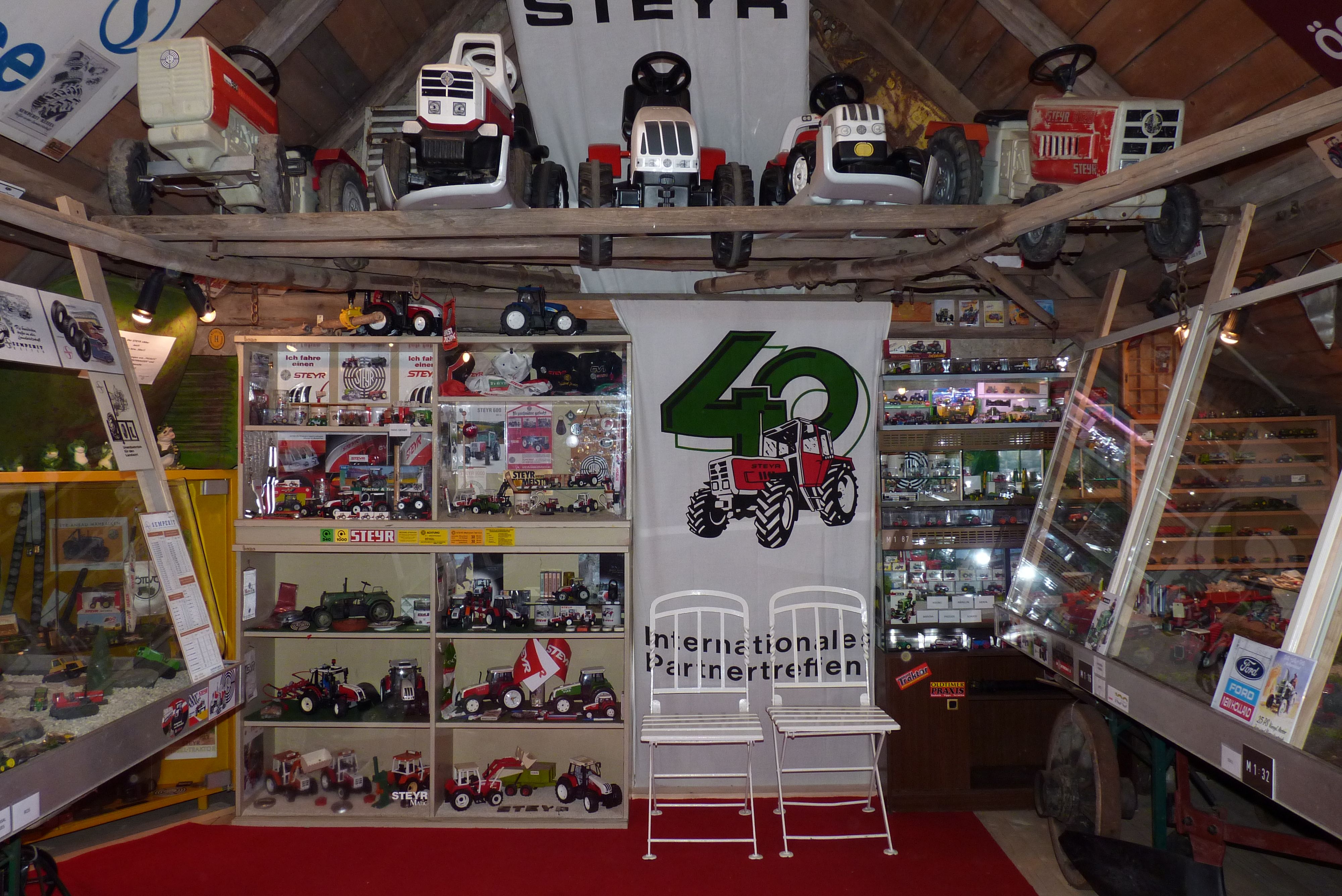 Ausstellung mit Steyr Traktormodellen und Spielzeugtraktoren in einem Raum mit Holzdecke.