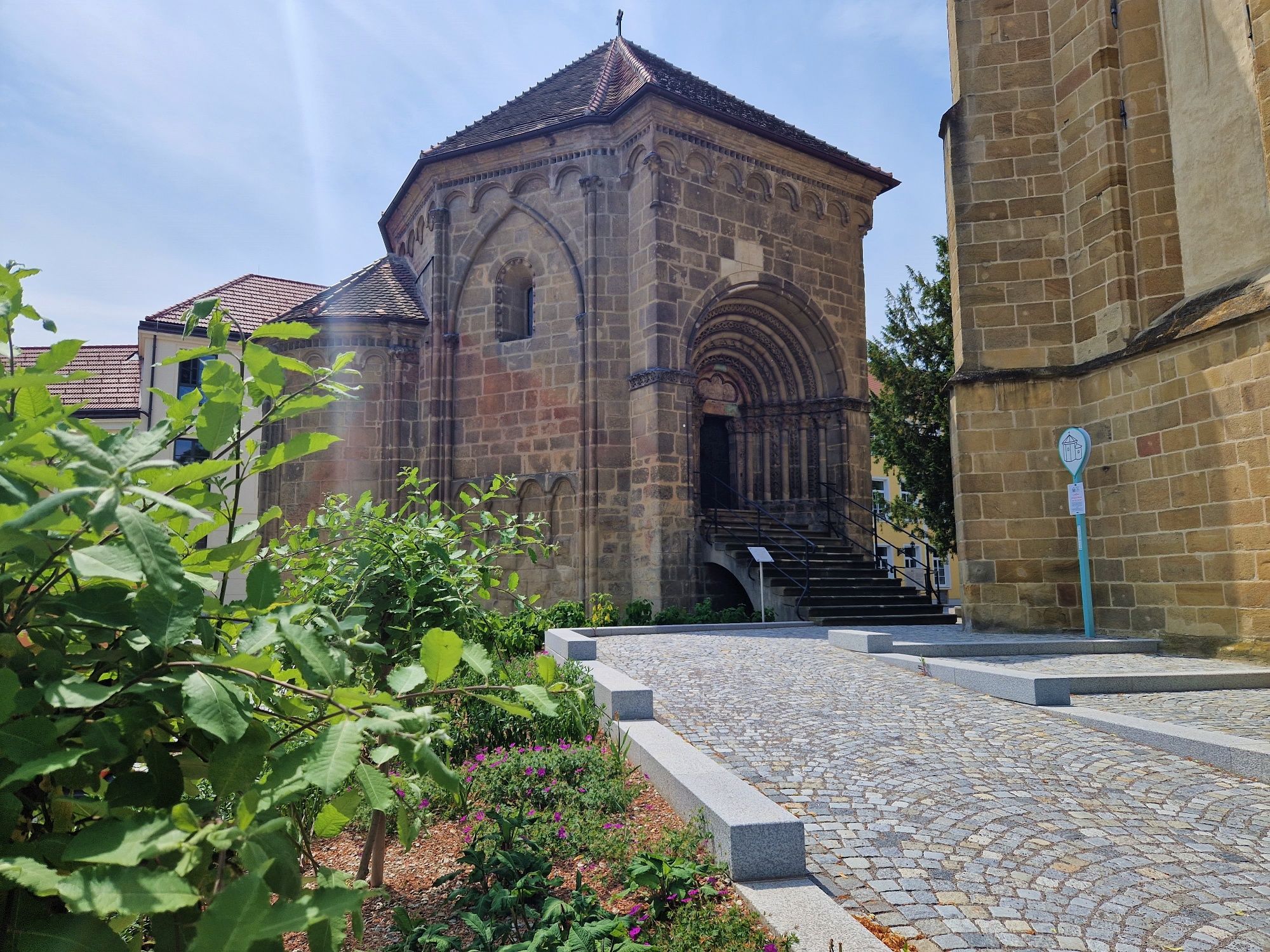 Historisches Gebäude mit romanischem Portal und Garten im Vordergrund.