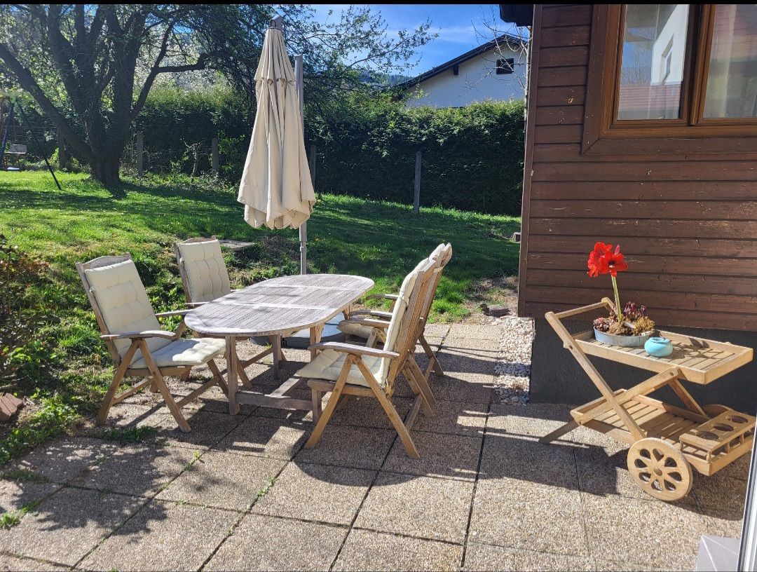 Terrasse mit Holzmöbeln und Sonnenschirm, umgeben von Garten.