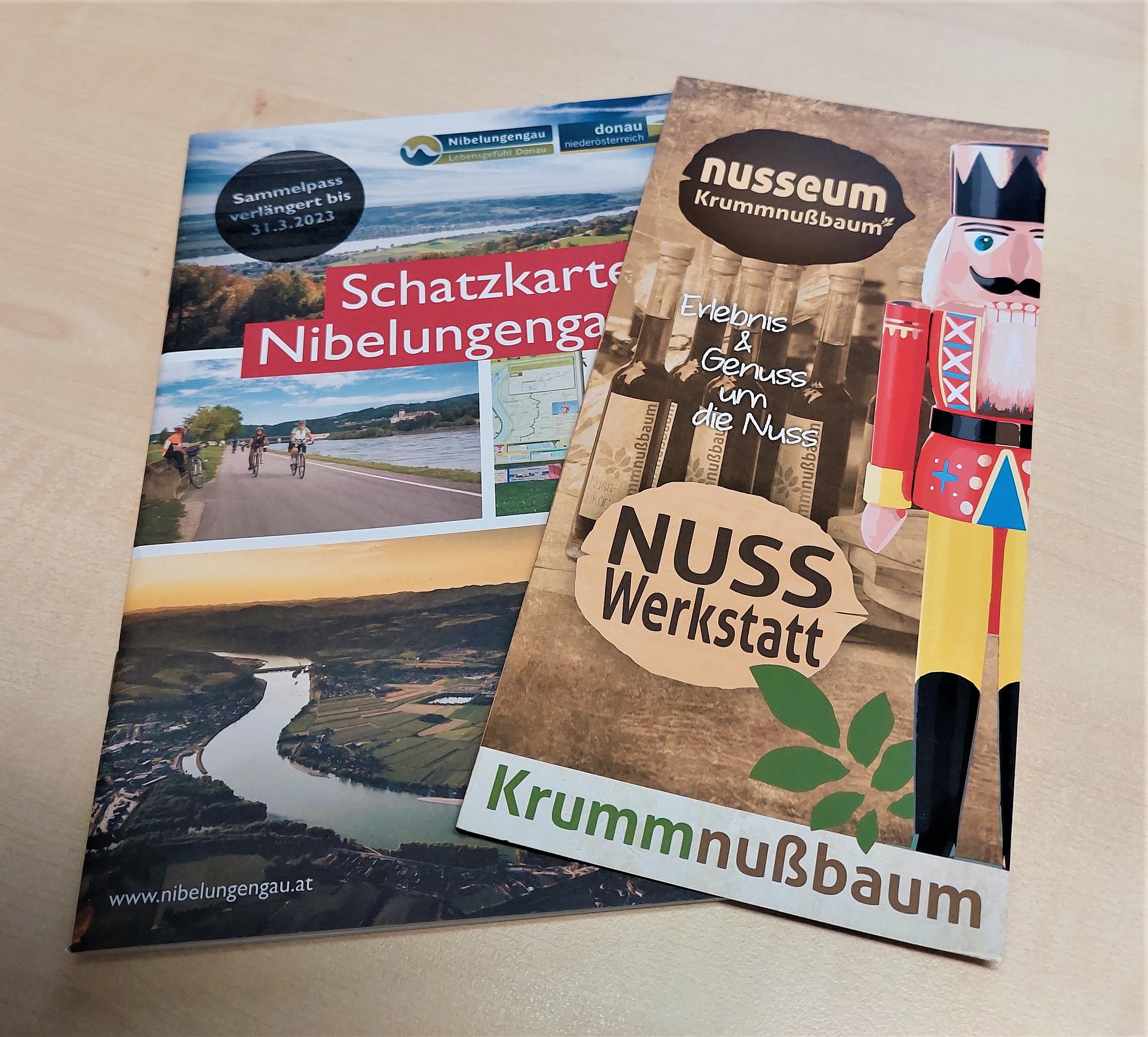 Zwei Broschüren auf einem Tisch: eine über die Nibelungengau Schatzkarte und eine über das Nusseum Krummnußbaum.