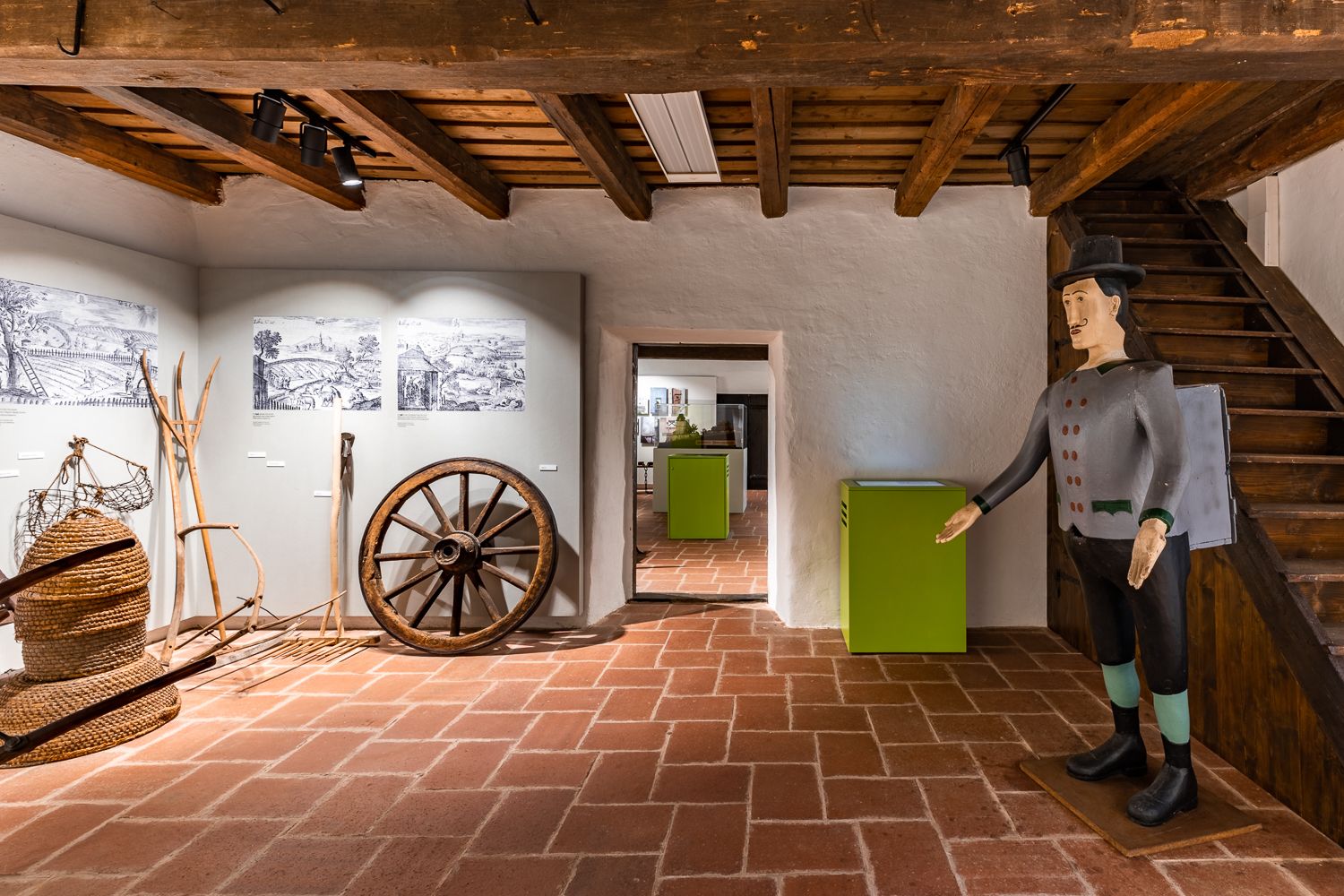 Innenansicht eines Museums mit alten landwirtschaftlichen Geräten und einer Holzfigur.