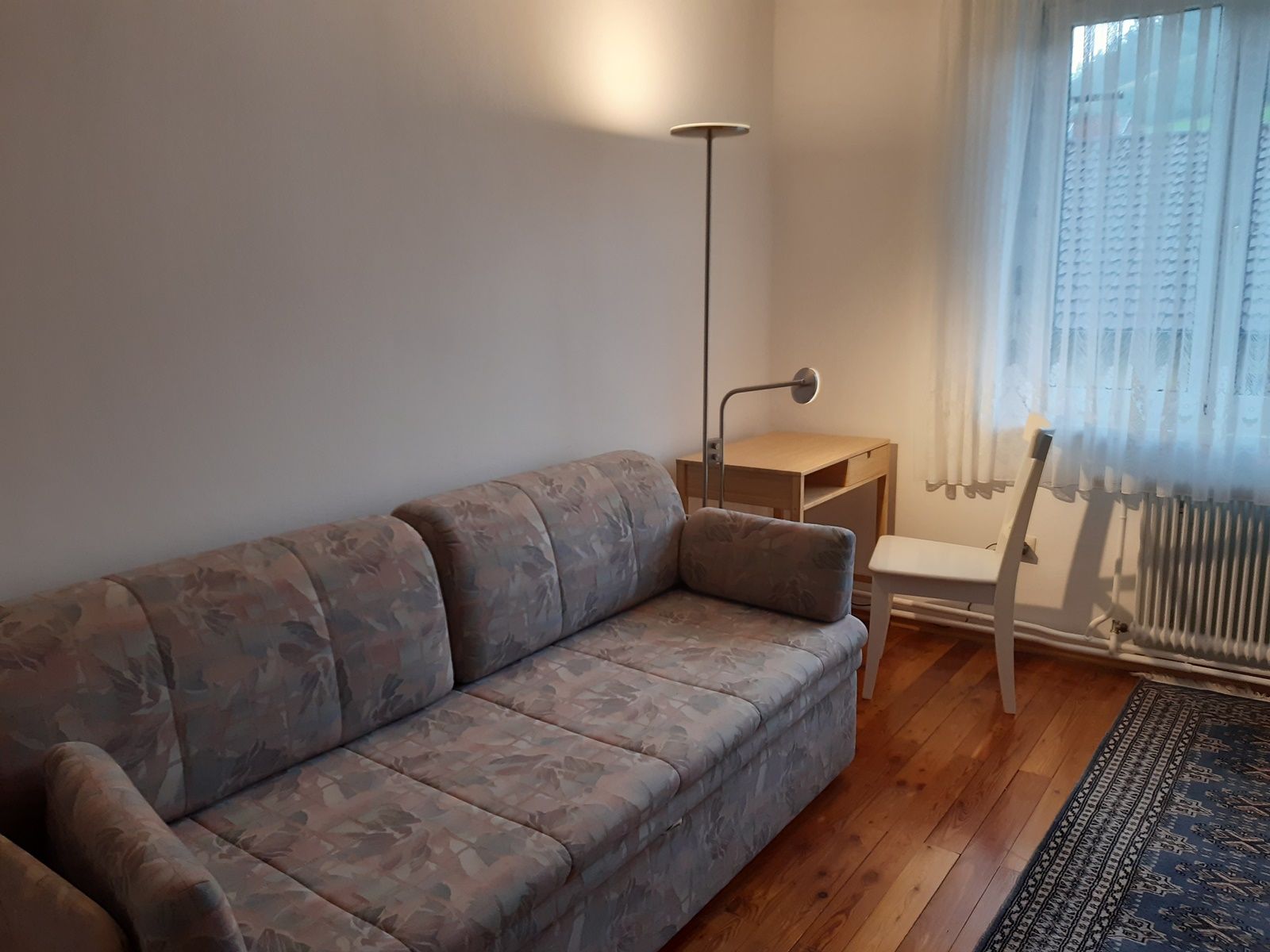 Zimmer mit ausziehbarer Couch, Schreibtisch und Stuhl.