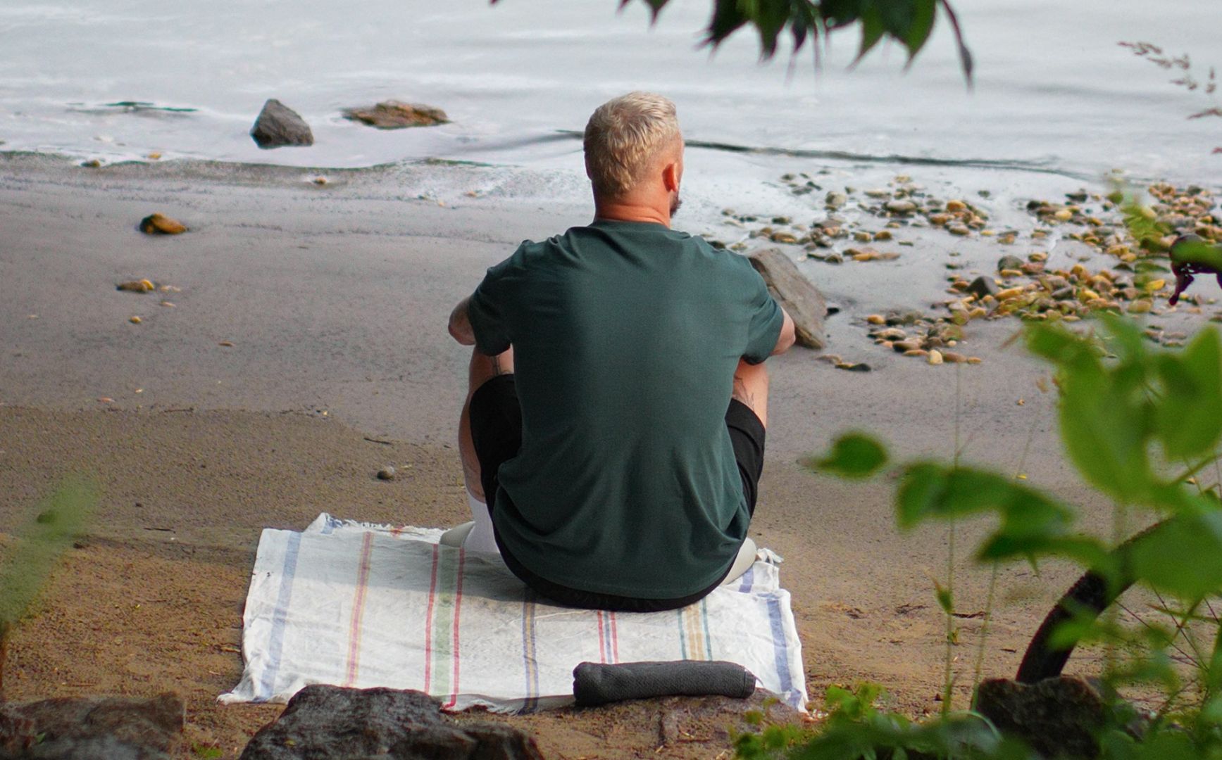 Person sitzt mit dem Rücken zur Kamera am Donaustrand Rossatz-Arnsdorf und blick auf das Wasser. 