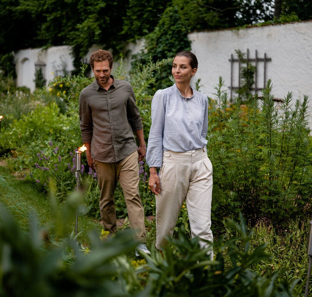In einer zauberhaften Gartenlandschaft schlendern zwei Personen unter dem sanften Licht des Vollmonds. Die üppigen Pflanzen und die sanften Farben der Natur schaffen eine friedliche Atmosphäre, die zum Verweilen einlädt. Ein perfekter Ort, um die Schönheit des Gartensommers zu genießen.