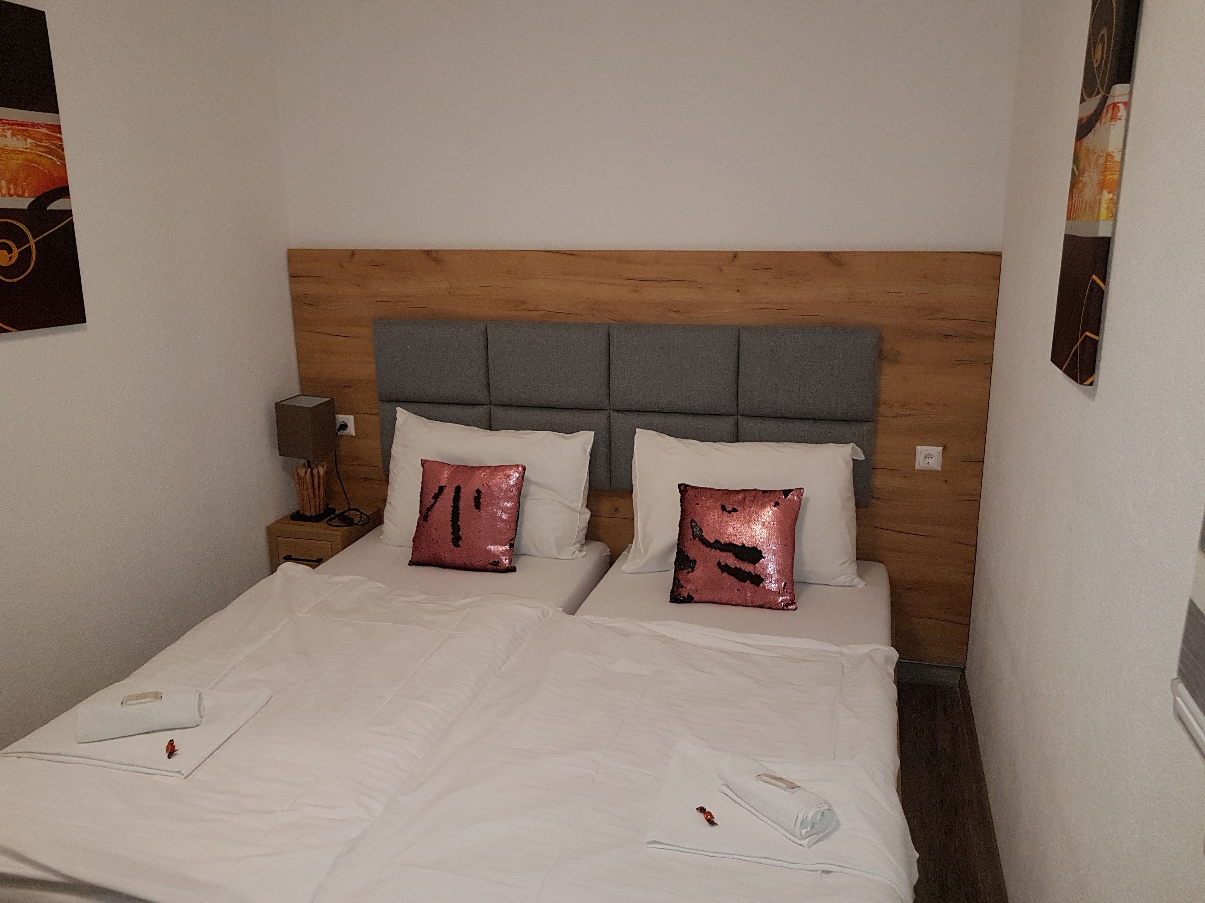 Doppelzimmer mit zwei Einzelbetten, grauem Kopfteil, rosa Pailletten-Kissen und weißer Bettwäsche.