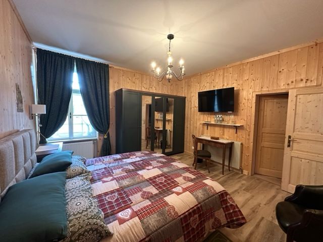 Gemütliches Hotelzimmer mit Holzwänden, Doppelbett, Schreibtisch, Kleiderschrank und Flachbildfernseher.