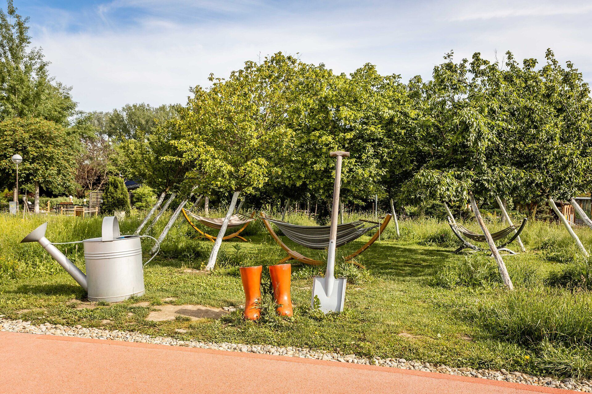 Inmitten einer blühenden Oase laden schaukelnde Hängematten und leuchtend orange Gummistiefel zum Entspannen ein. Der Duft von frischem Gras und blühenden Pflanzen erfüllt die Luft, während das sanfte Plätschern des Wassers eine beruhigende Atmosphäre schafft. Ein perfekter Ort, um die Schönheit des Frühlings zu genießen und die Seele baumeln zu lassen.
