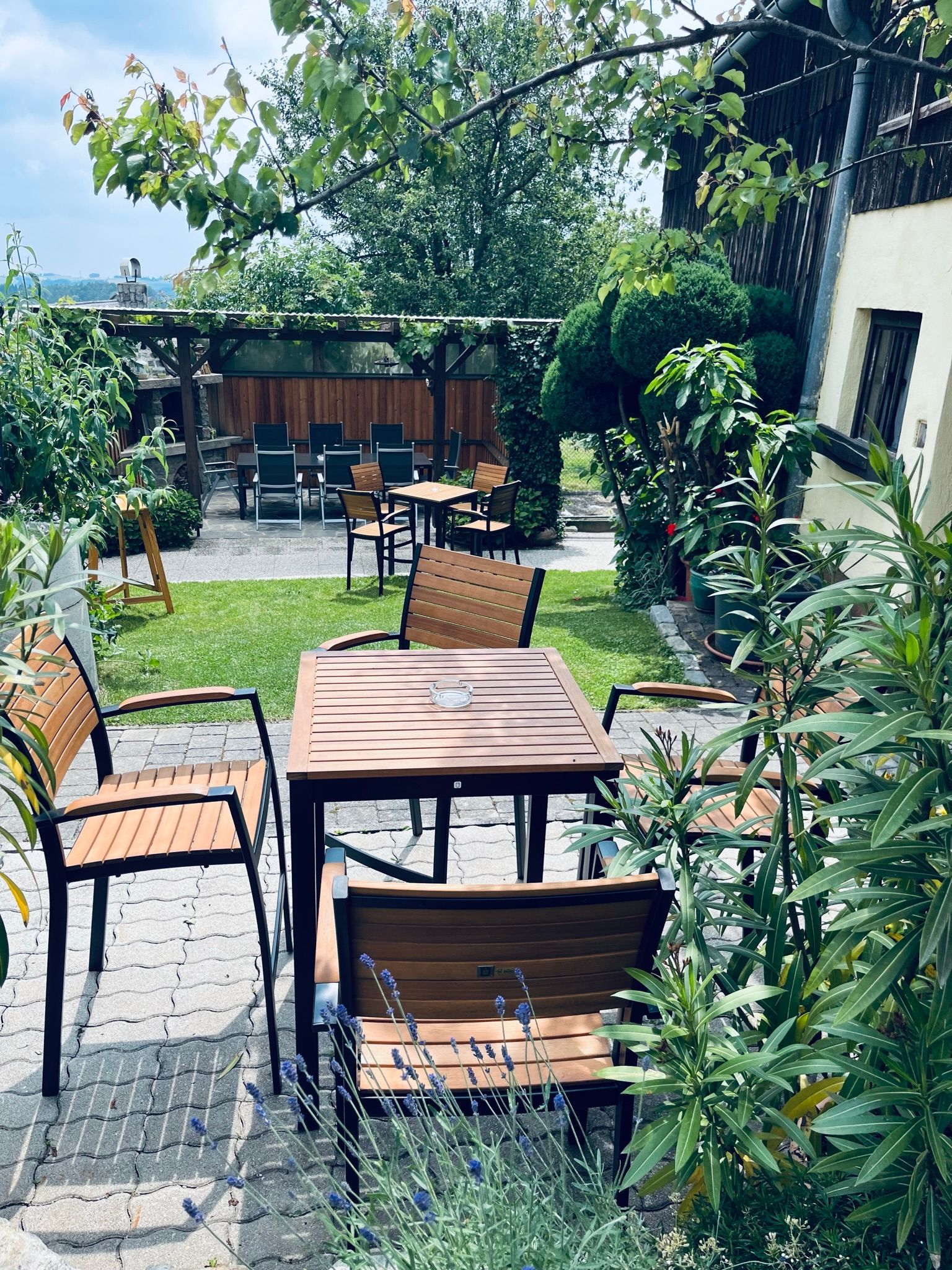 Ein gemütlicher Gastgarten mit Holztischen und -stühlen, umgeben von üppigem Grün und Pflanzen.