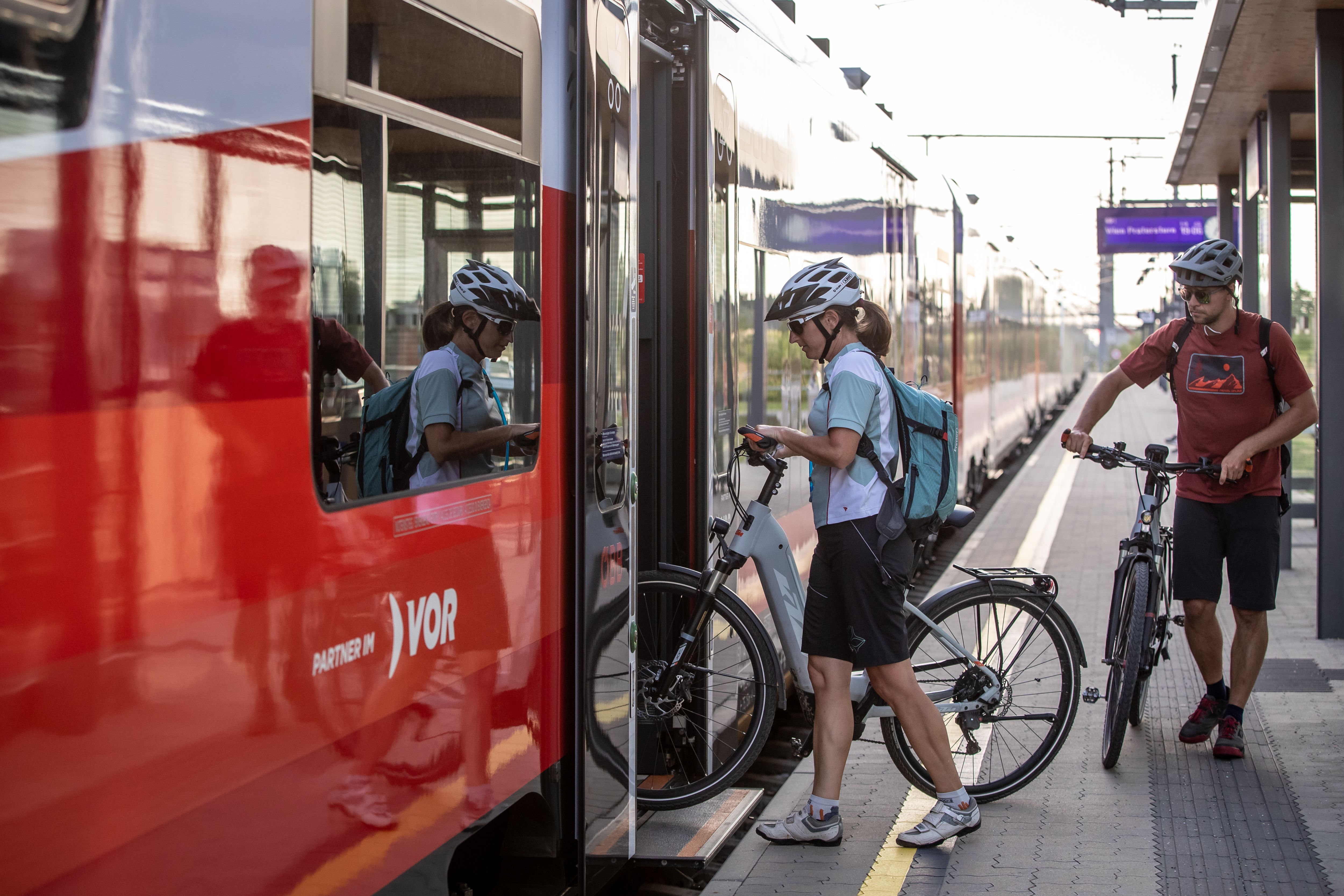 Zwei Radfahrer steigen mit ihren Fahrrädern in einen Zug ein.