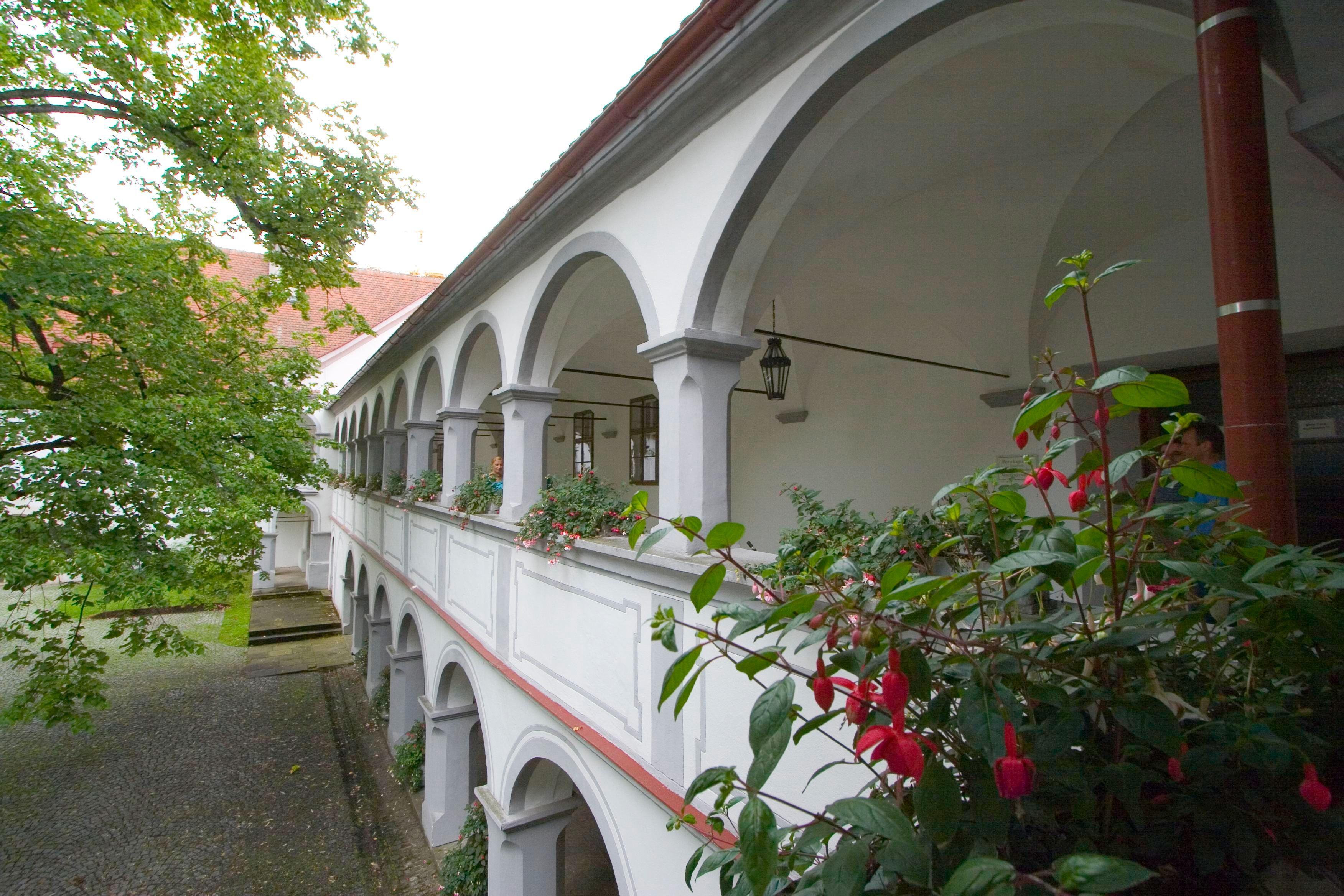 Ein zweistöckiger Arkadengang mit weißen Bögen und Blumen im Schloss Scheibbs.
