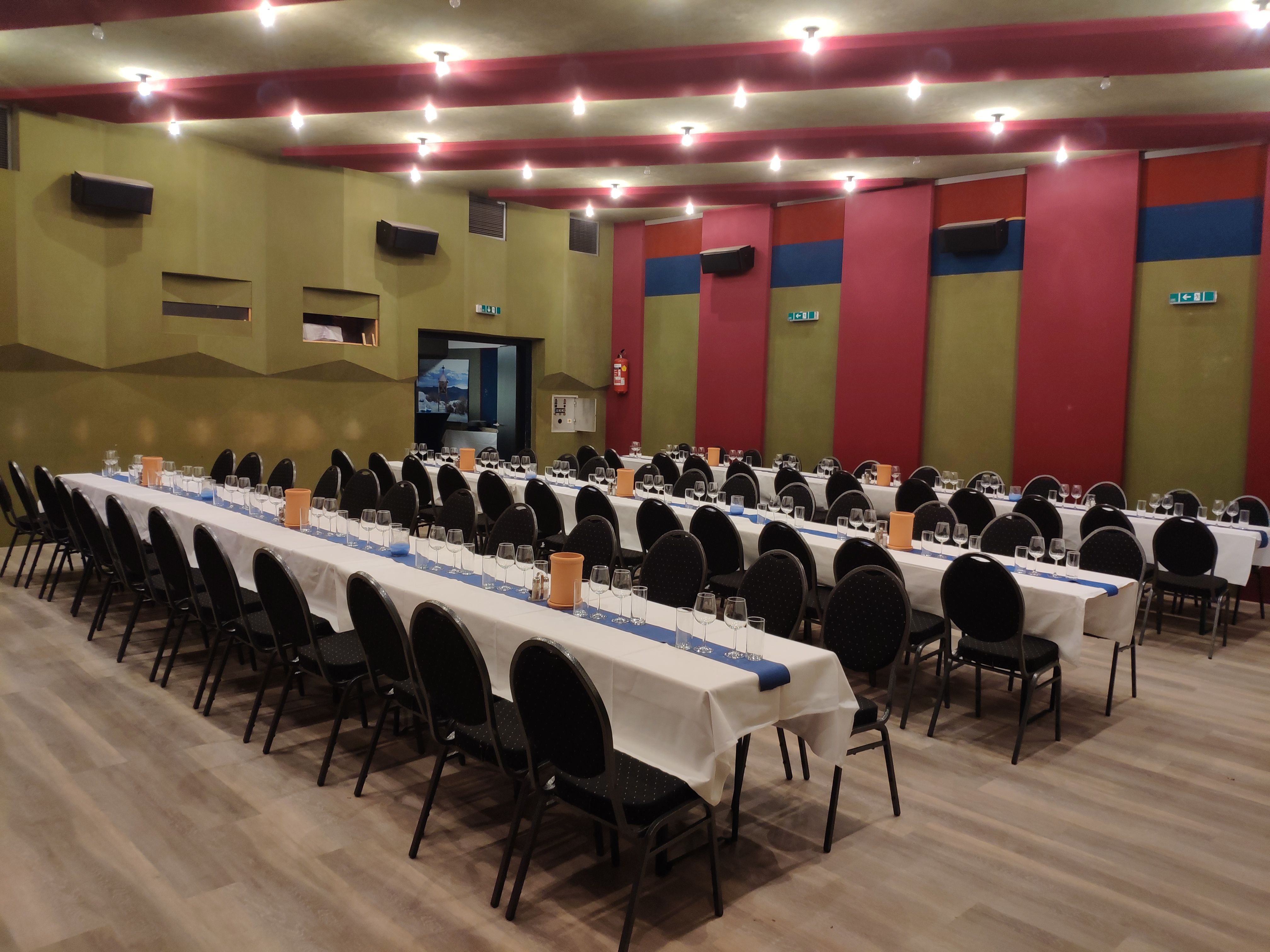 Ein großer Saal mit langen, gedeckten Tischen und schwarzen Stühlen, bereit für ein Event.