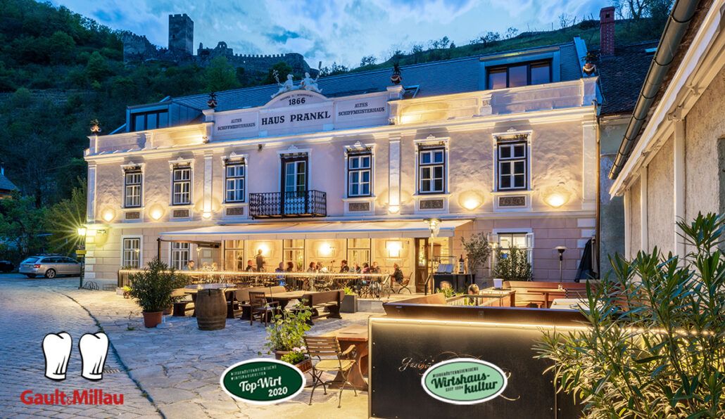 Abendaufnahme des Gasthofs Prankl mit beleuchteter Fassade und Gästen auf der Terrasse.