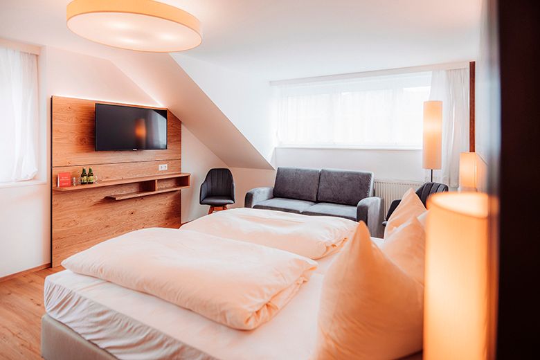 Modernes Hotelzimmer mit Doppelbett, Sofa, TV und stilvoller Beleuchtung.