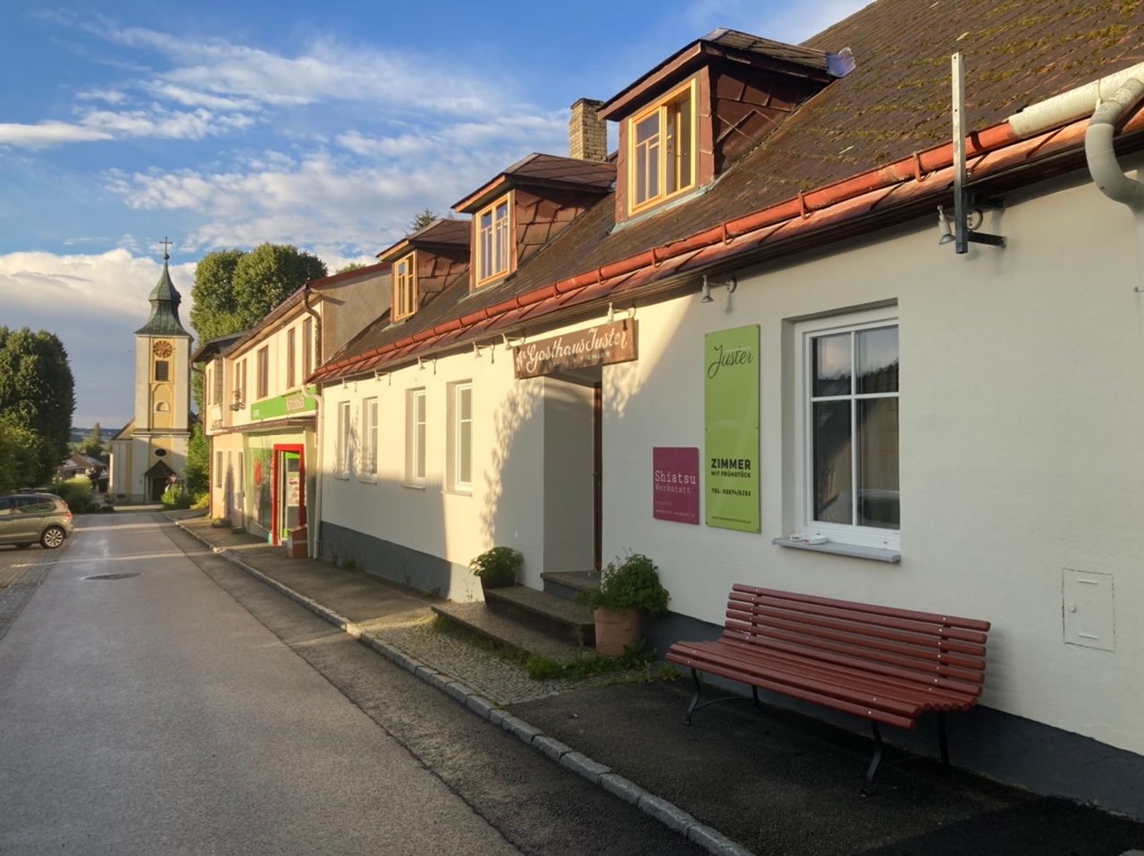 Außenansicht des Bühnenwirtshauses Juster mit einer Kirche im Hintergrund.