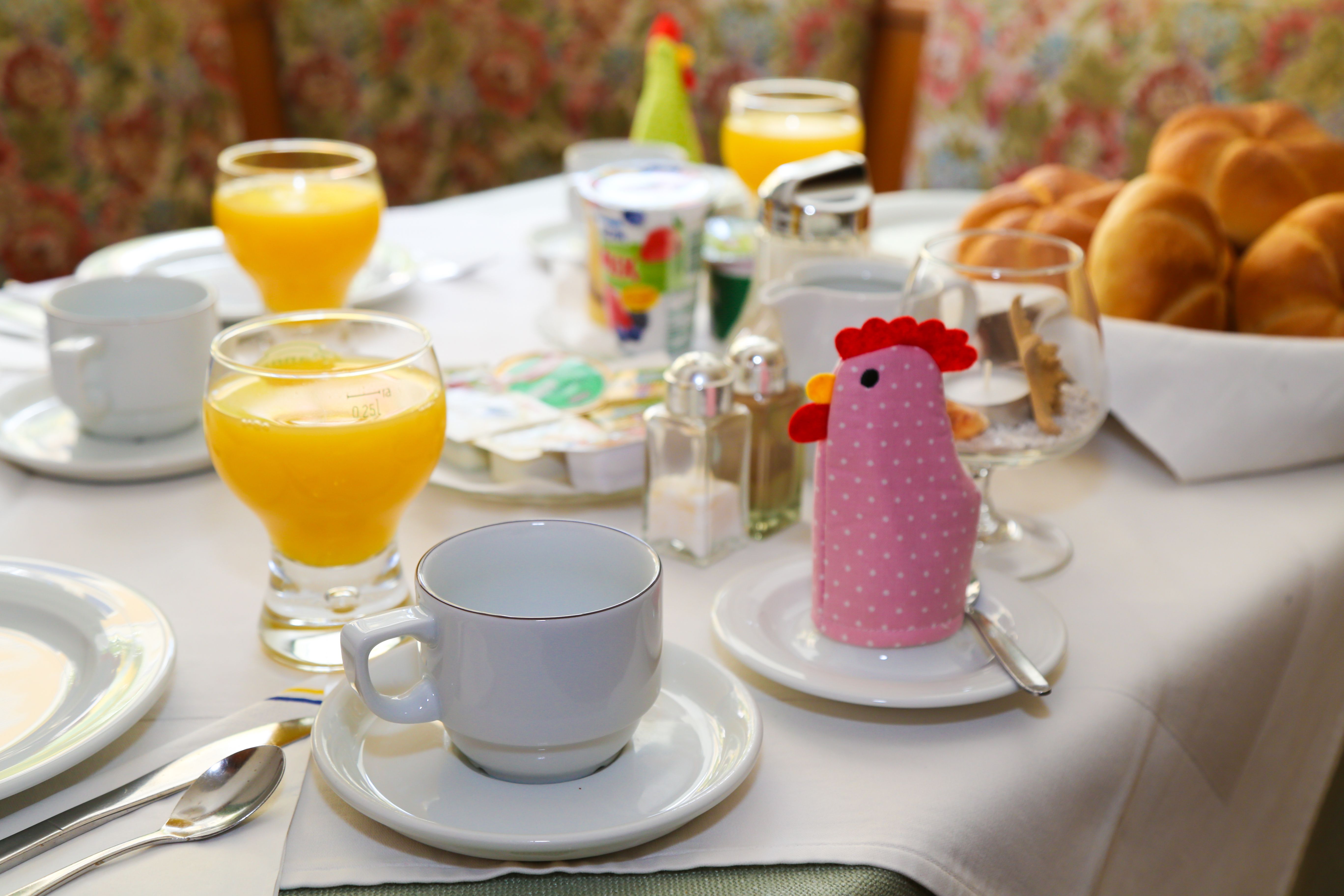 Frühstückstisch mit Orangensaft, Brötchen und Tassen in einer Pension.
