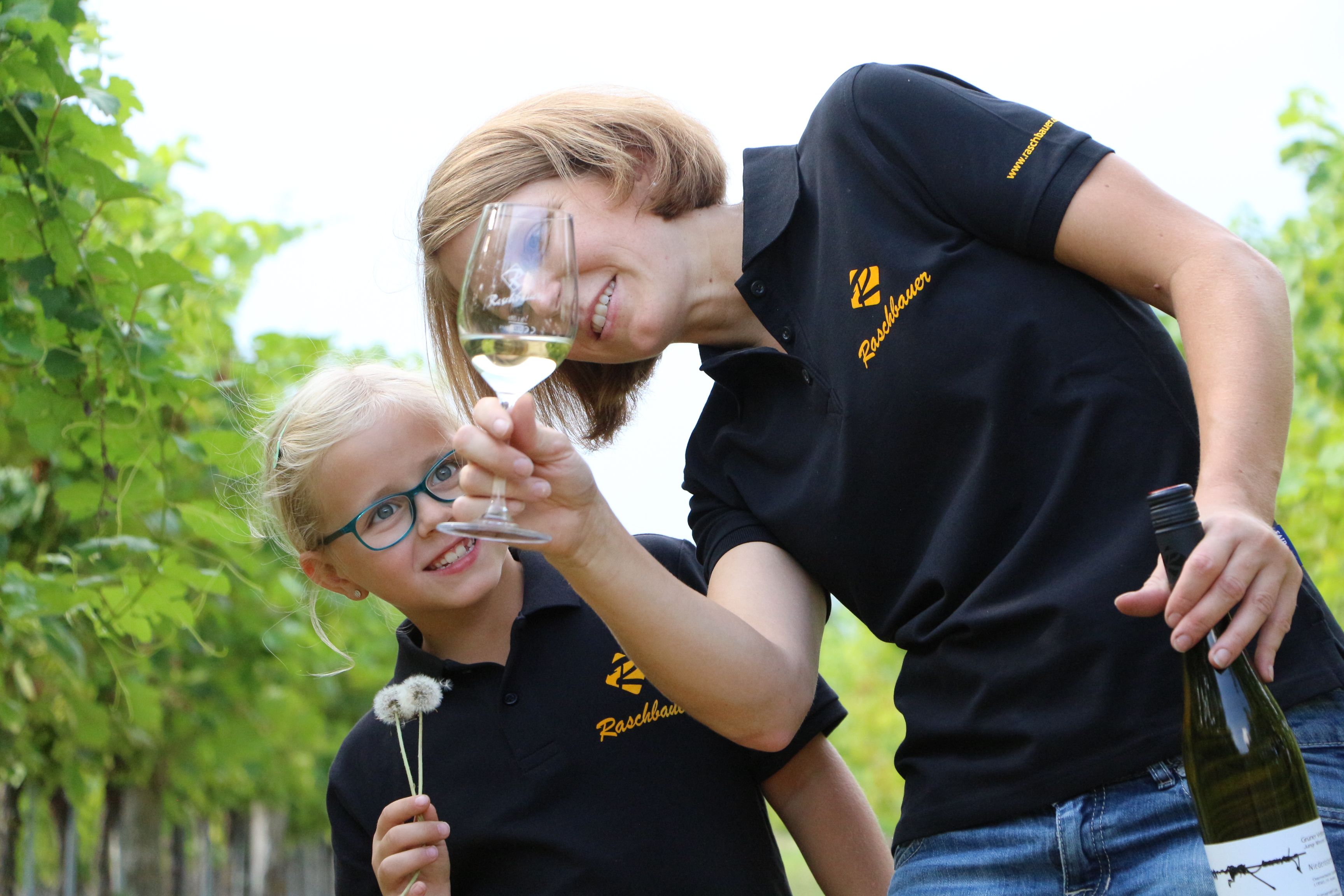Frau und Kind im Weinberg mit Weinglas und Pusteblume.