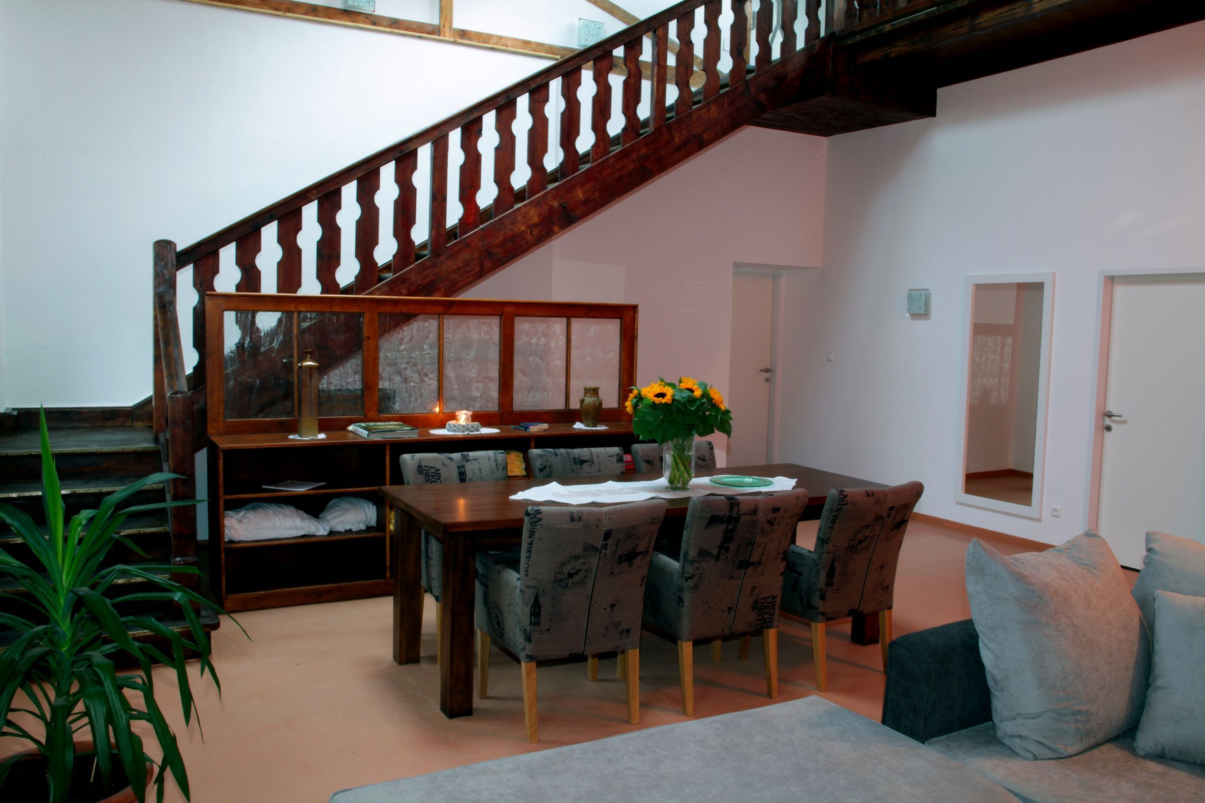 Essbereich in einem Loft mit Holztisch, Stühlen, Treppe und Pflanzen.