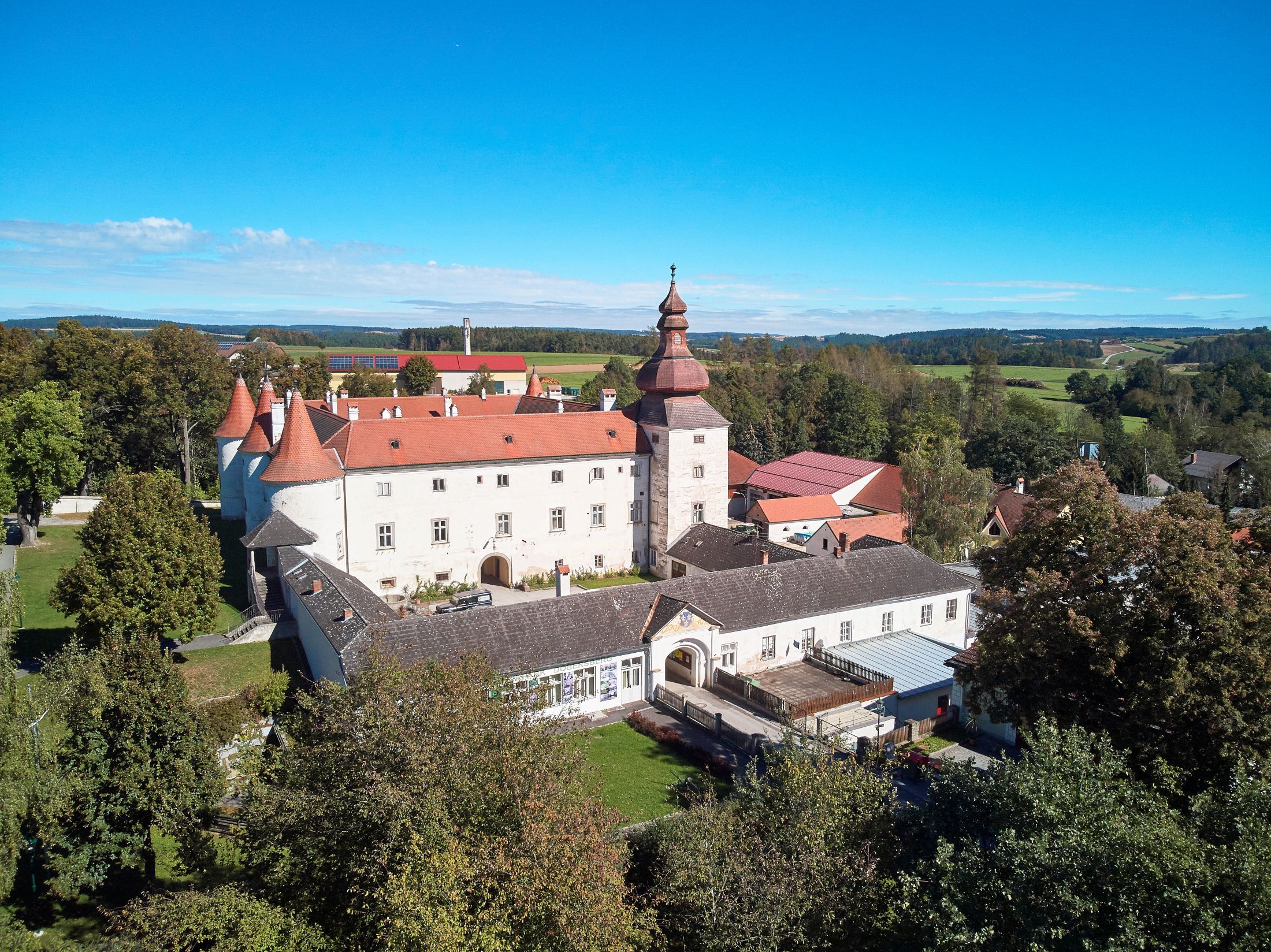 Luftaufnahme von Schloss Dobersberg mit rotem Dach und umliegender Landschaft.