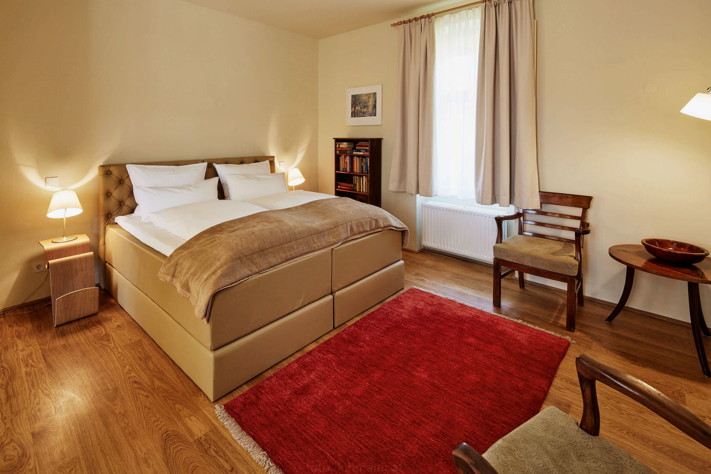 Ein gemütliches Schlafzimmer mit einem großen Bett, zwei Nachttischen mit Lampen, einem roten Teppich und Holzmöbeln.