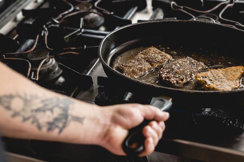 Person brät Fischstücke in einer Pfanne auf einem Herd.
