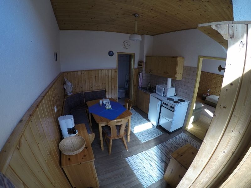 Wohnküche in einer Ferienwohnung mit Holzmöbeln, Esstisch, Küchenzeile und Zugang zu einem Schlafzimmer.