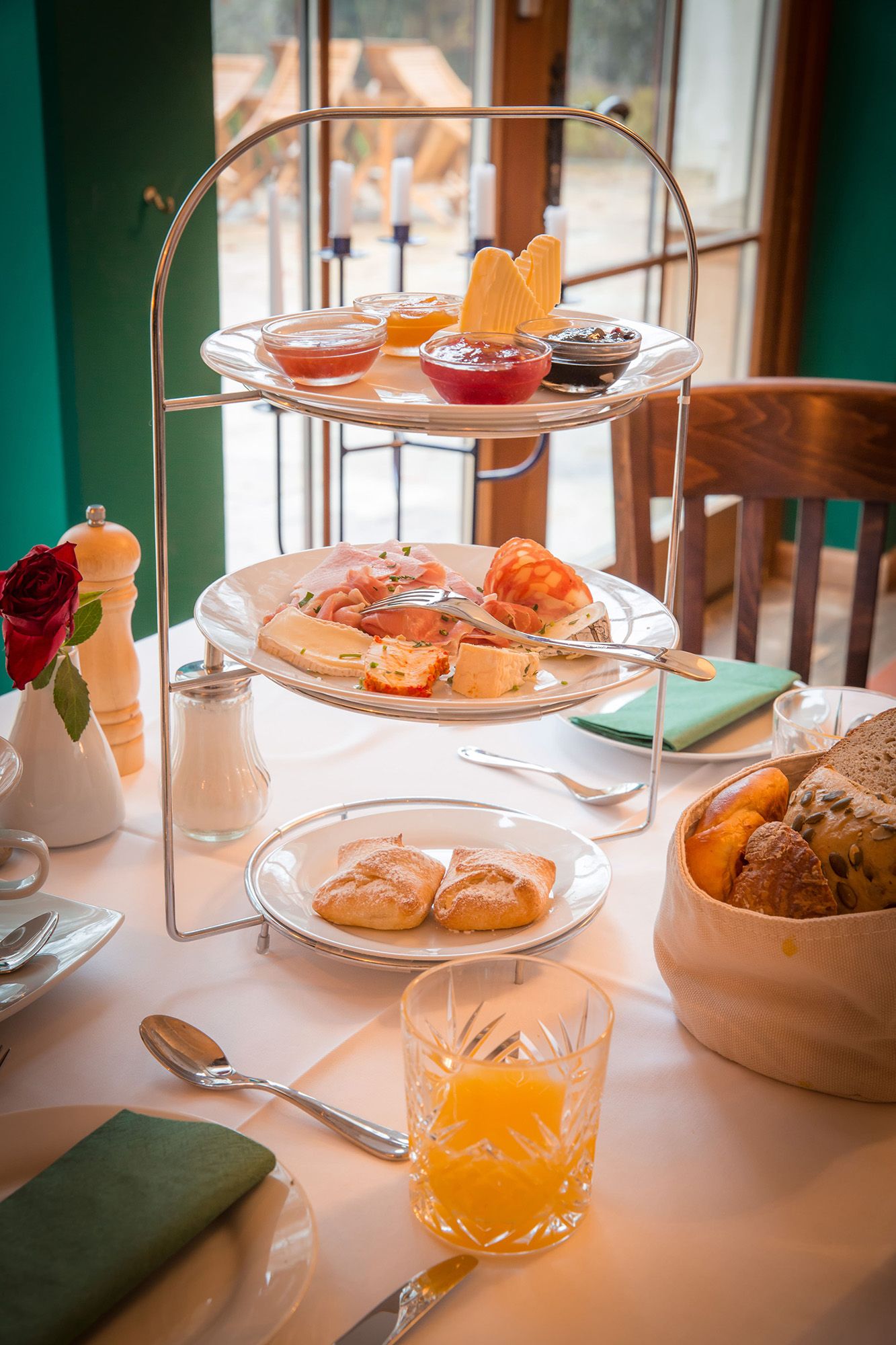 Ein Frühstückstisch mit einer Etagere voller Aufschnitt, Marmeladen und Brötchen, daneben ein Glas Orangensaft.