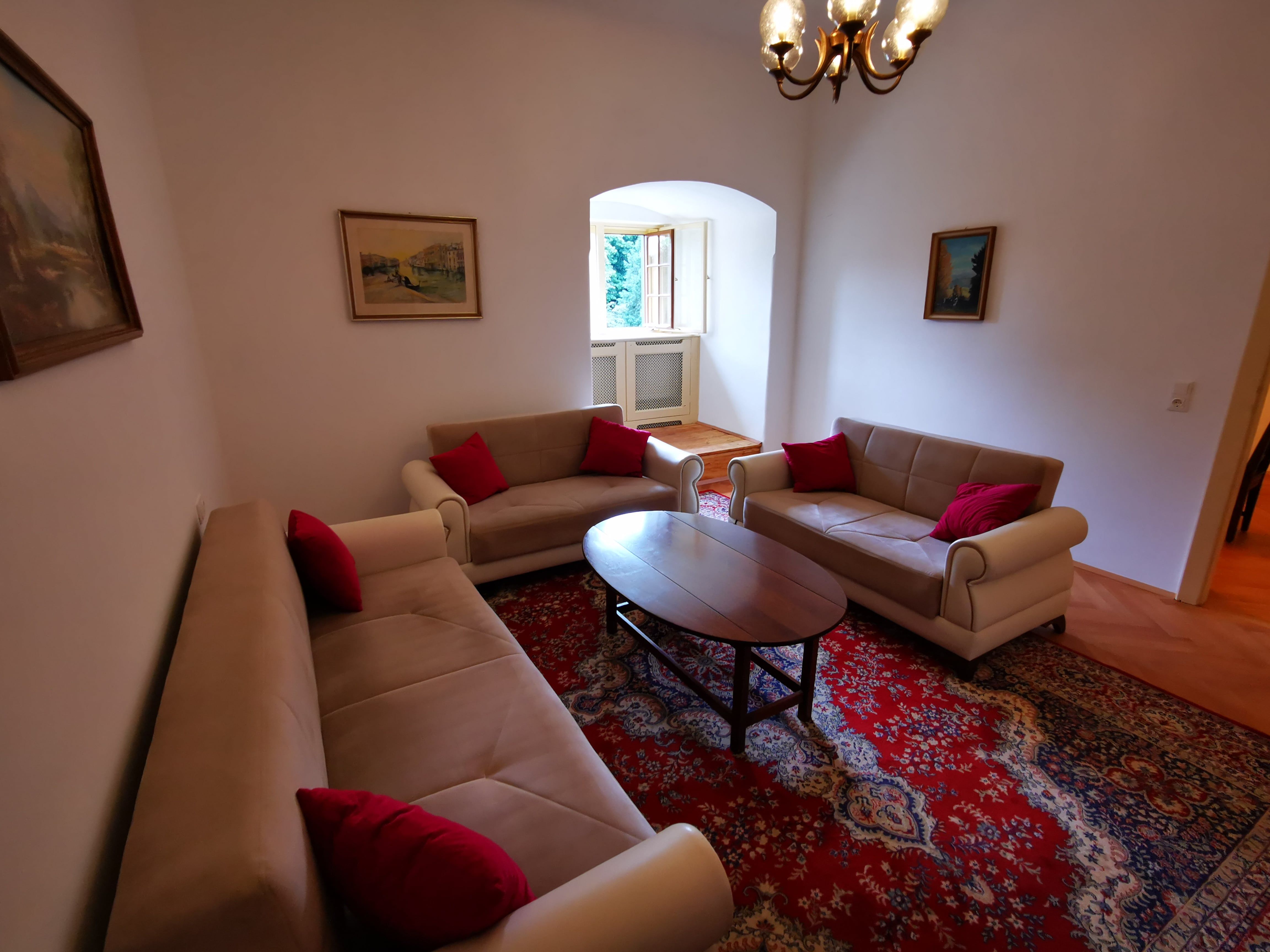 Wohnzimmer mit drei Sofas, rotem Teppich und Gemälden an den Wänden.