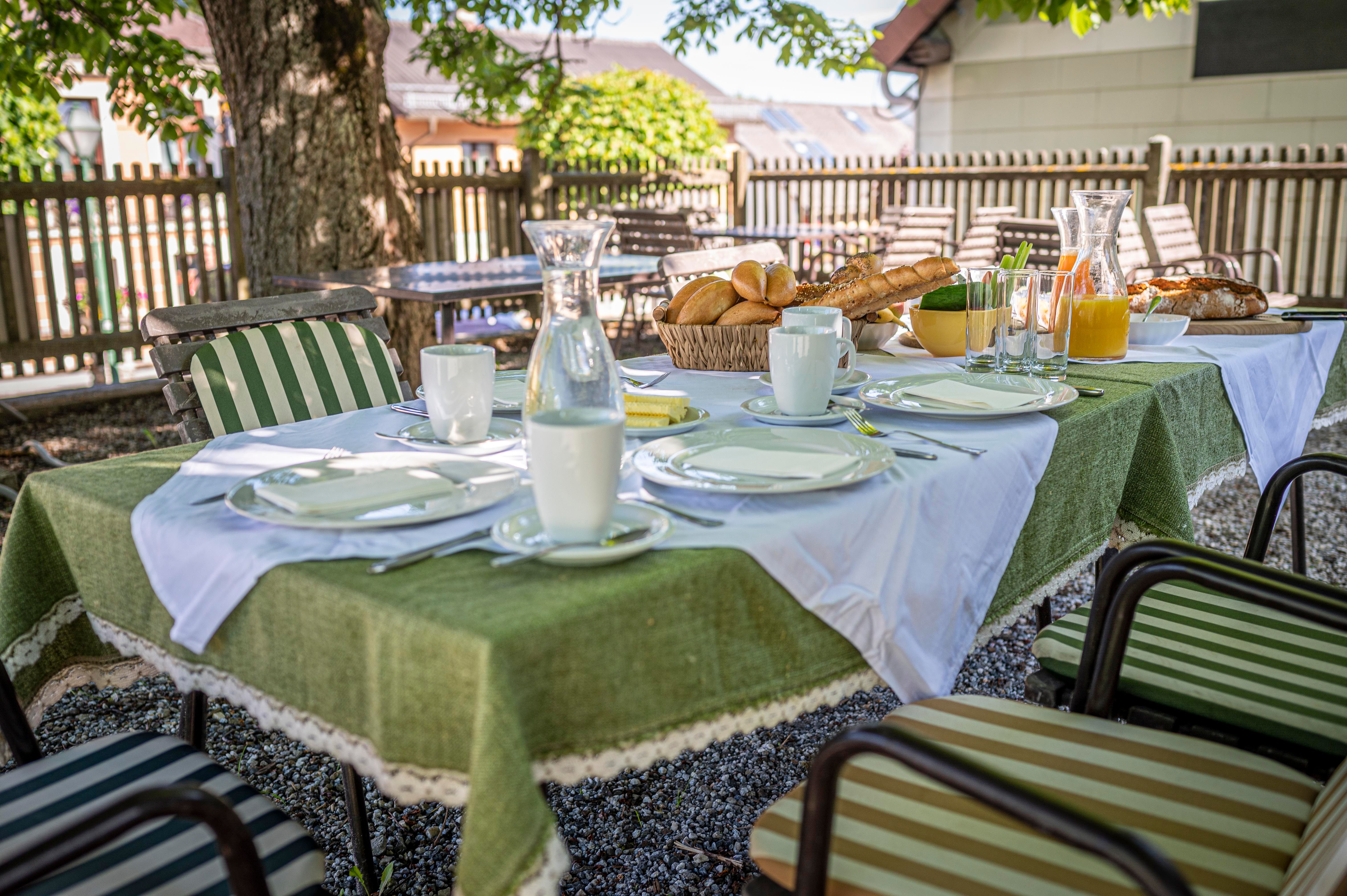 Ein gedeckter Tisch im Freien mit Geschirr, Brot, Saft und Milch unter einem Baum.