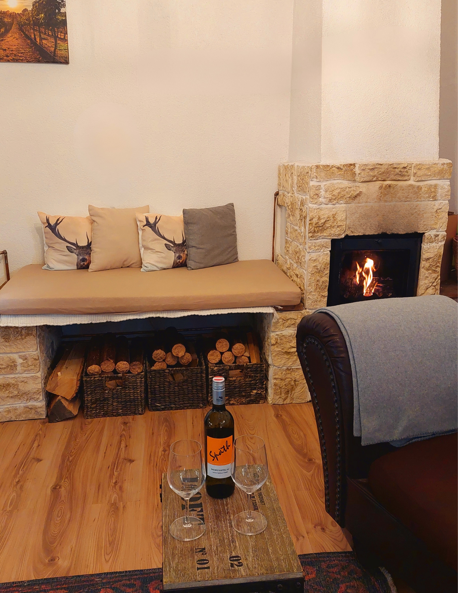 Gemütliche Sitzecke mit Kamin, Weinflasche und Gläsern auf einem Holztisch.